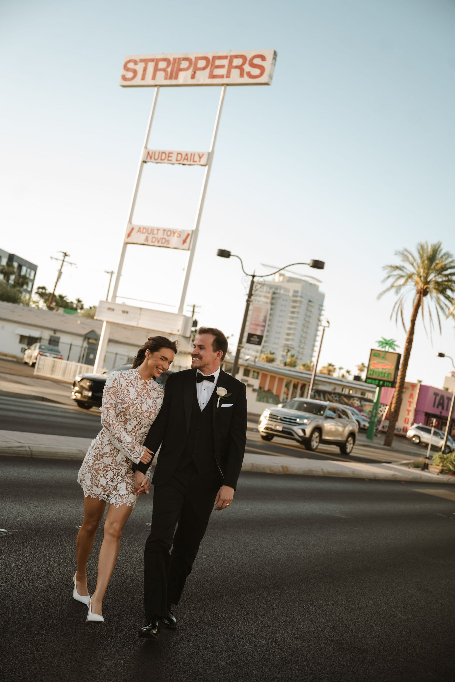 Newlywed couple walking and laughing in front of a Strippers sign on the Las Vegas Strip.