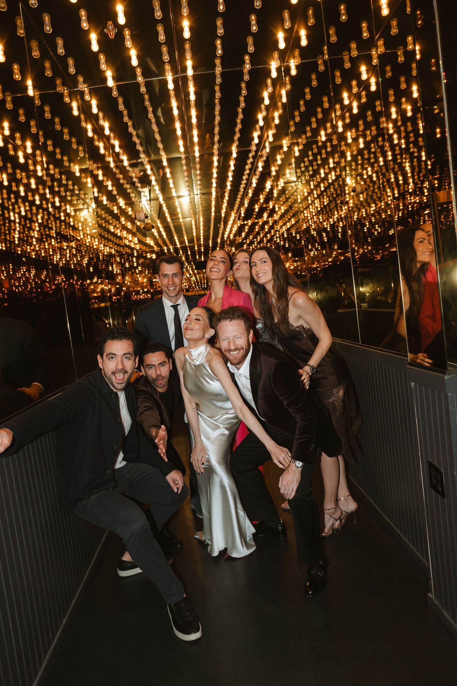 Wedding guests dance and celebrate under a stunning canopy of glowing string lights at an evening reception.