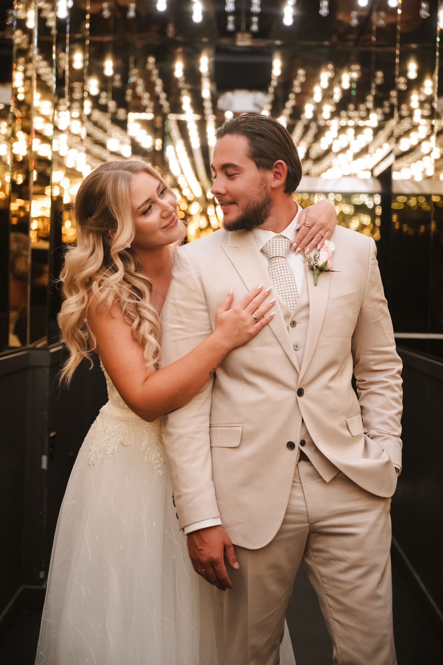Newlyweds in white and cream attire sharing romantic moments under string lights.