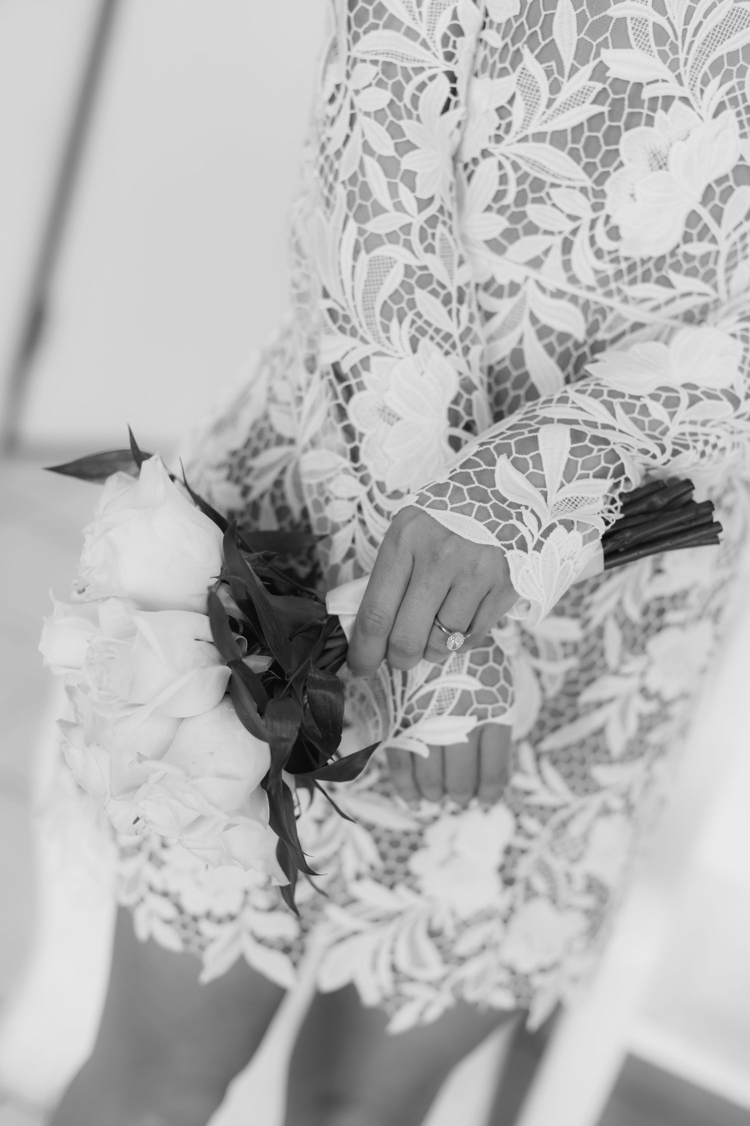 Bride in lace wedding dress holding a bouquet of roses, black and white photo.