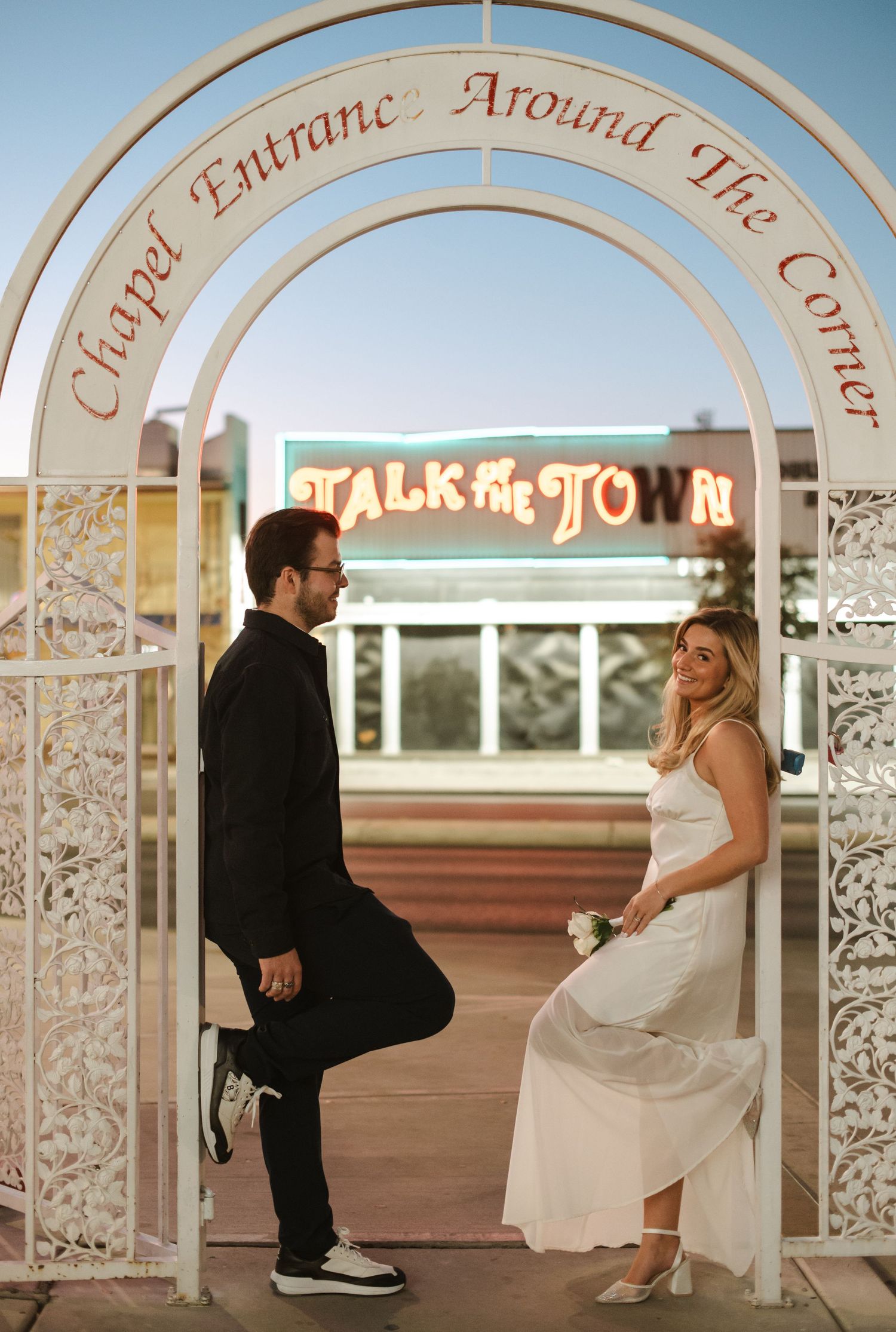 A couple dances under decorative white arches at sunset.