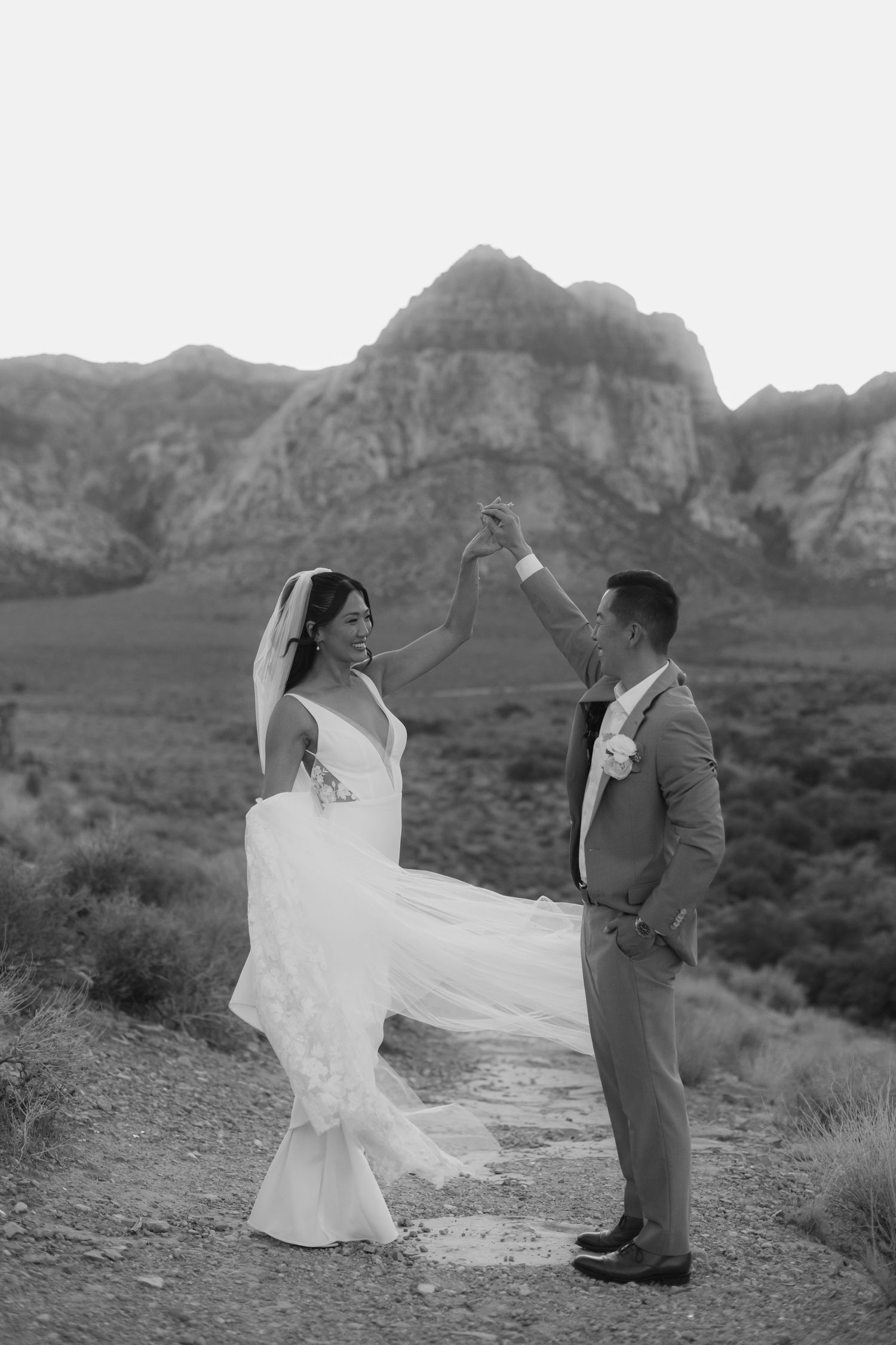 Black and white photo of a bride and groom dancing outdoors with rocky mountains in the background.
