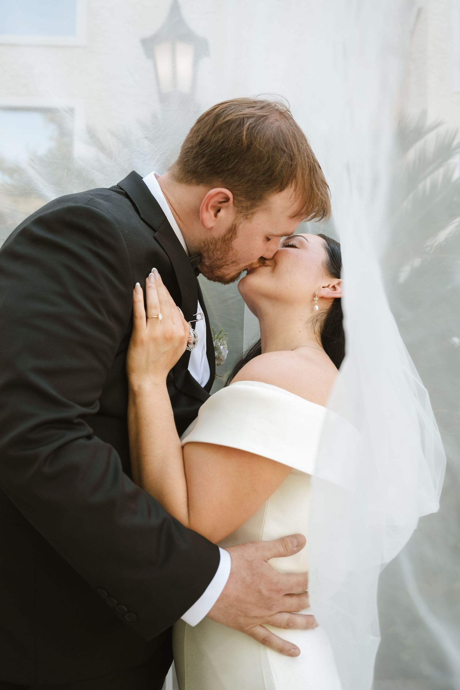 A bride and groom share a romantic kiss under a flowing white veil on their wedding day.