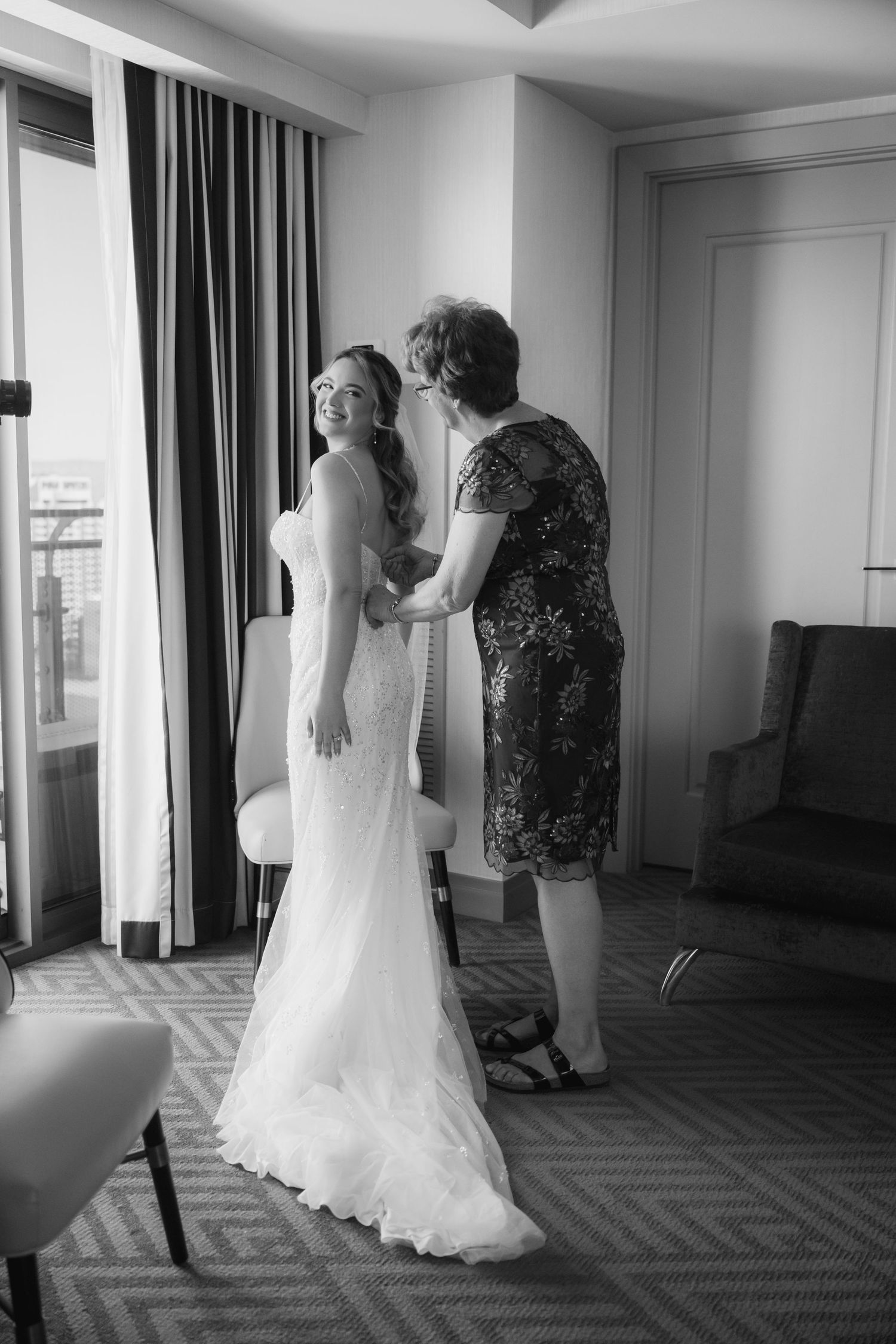 A wedding dress fitting moment captured in black and white in a hotel room.