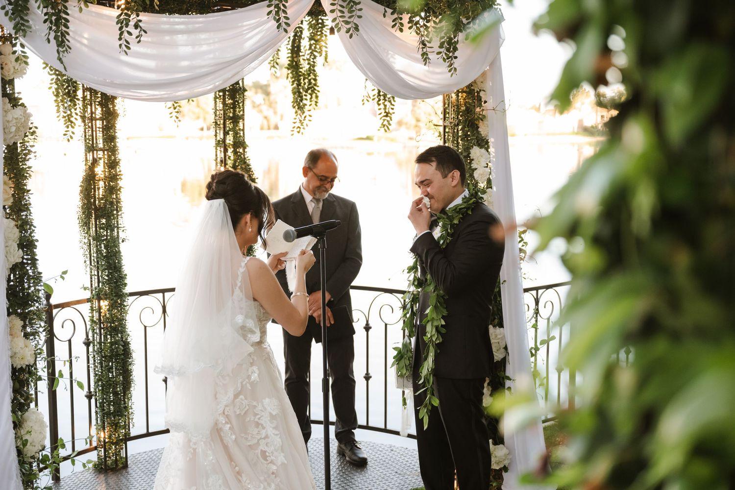 Bride and groom exchange vows under floral arch with greenery at elegant outdoor wedding ceremony.