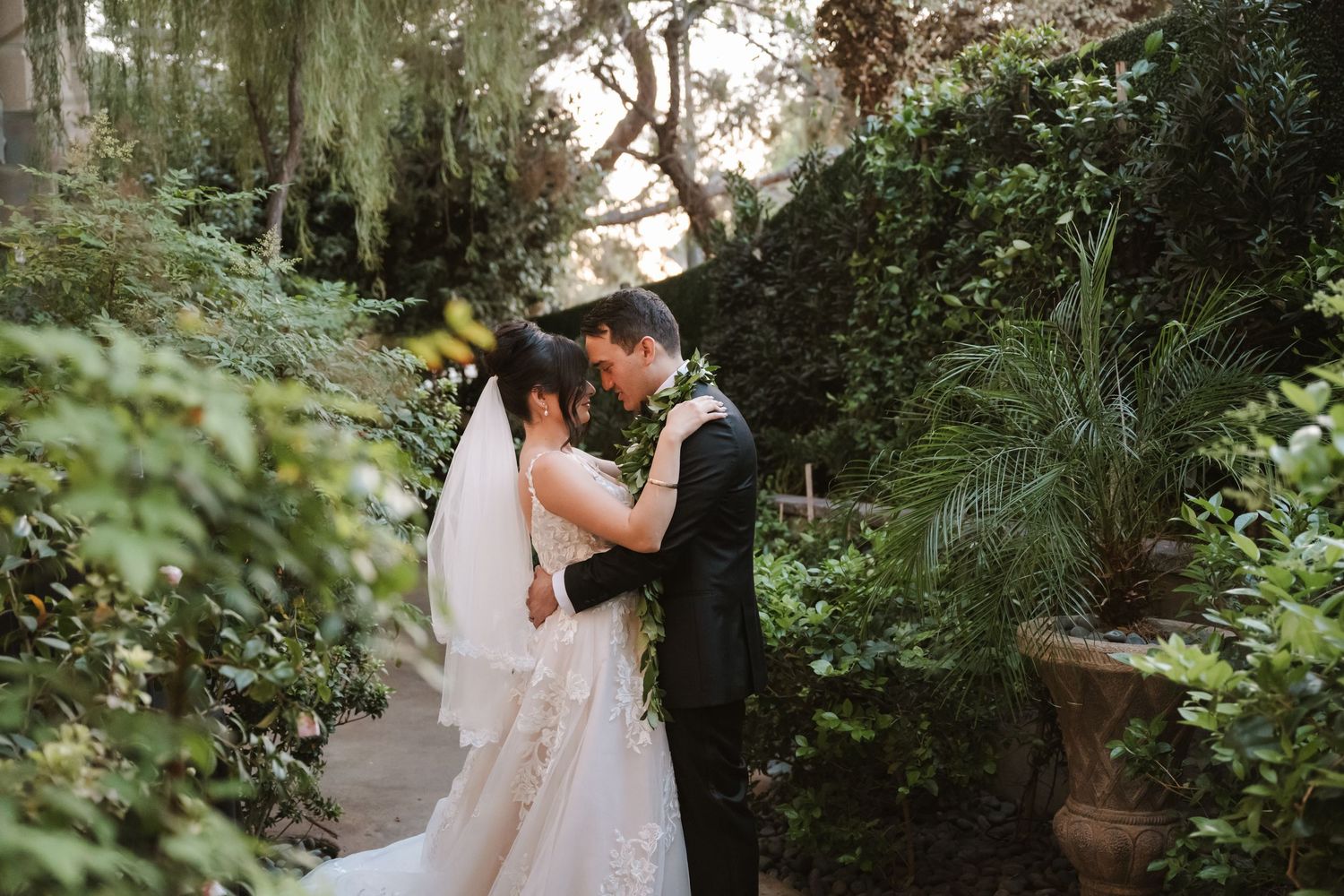 Bride and groom share a romantic moment surrounded by lush greenery in a garden wedding setting.