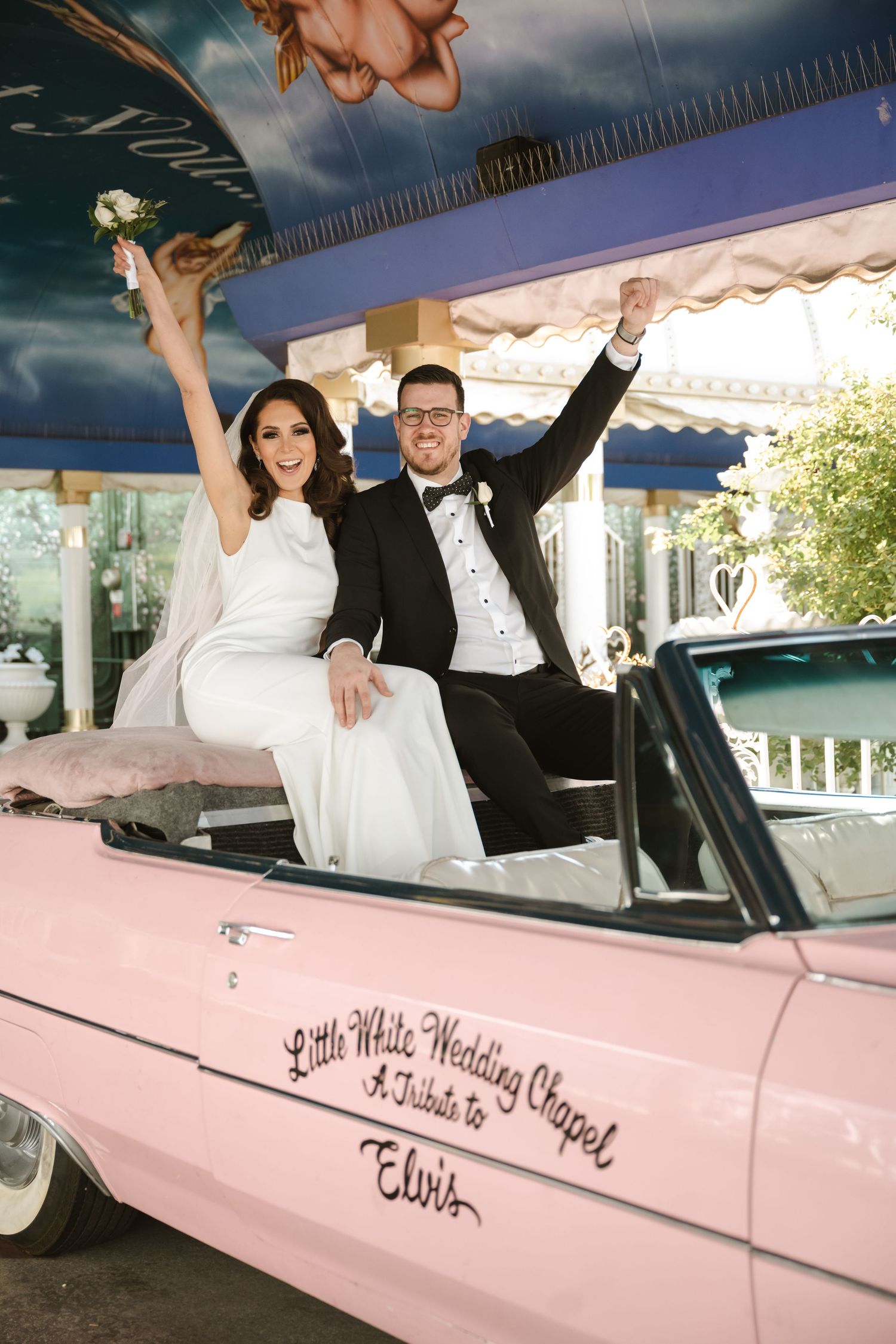 Joyful wedding couple celebrating in a classic pink convertible car.