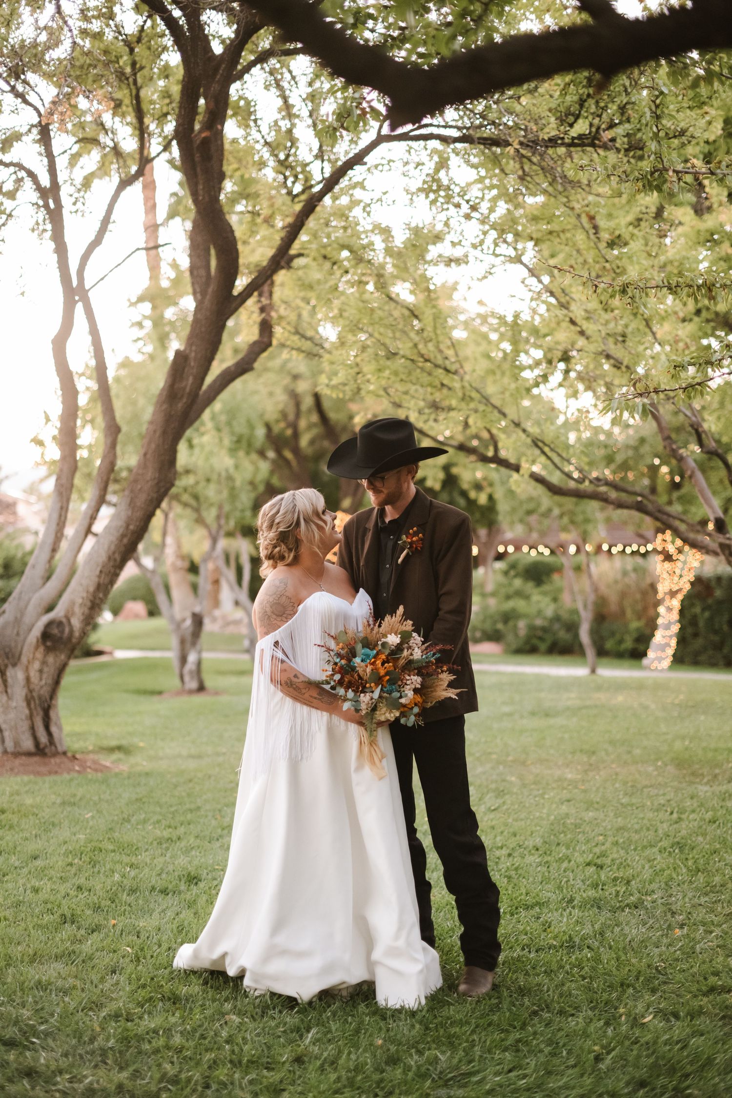 A romantic outdoor wedding photoshoot in a park with large trees creating a natural backdrop.