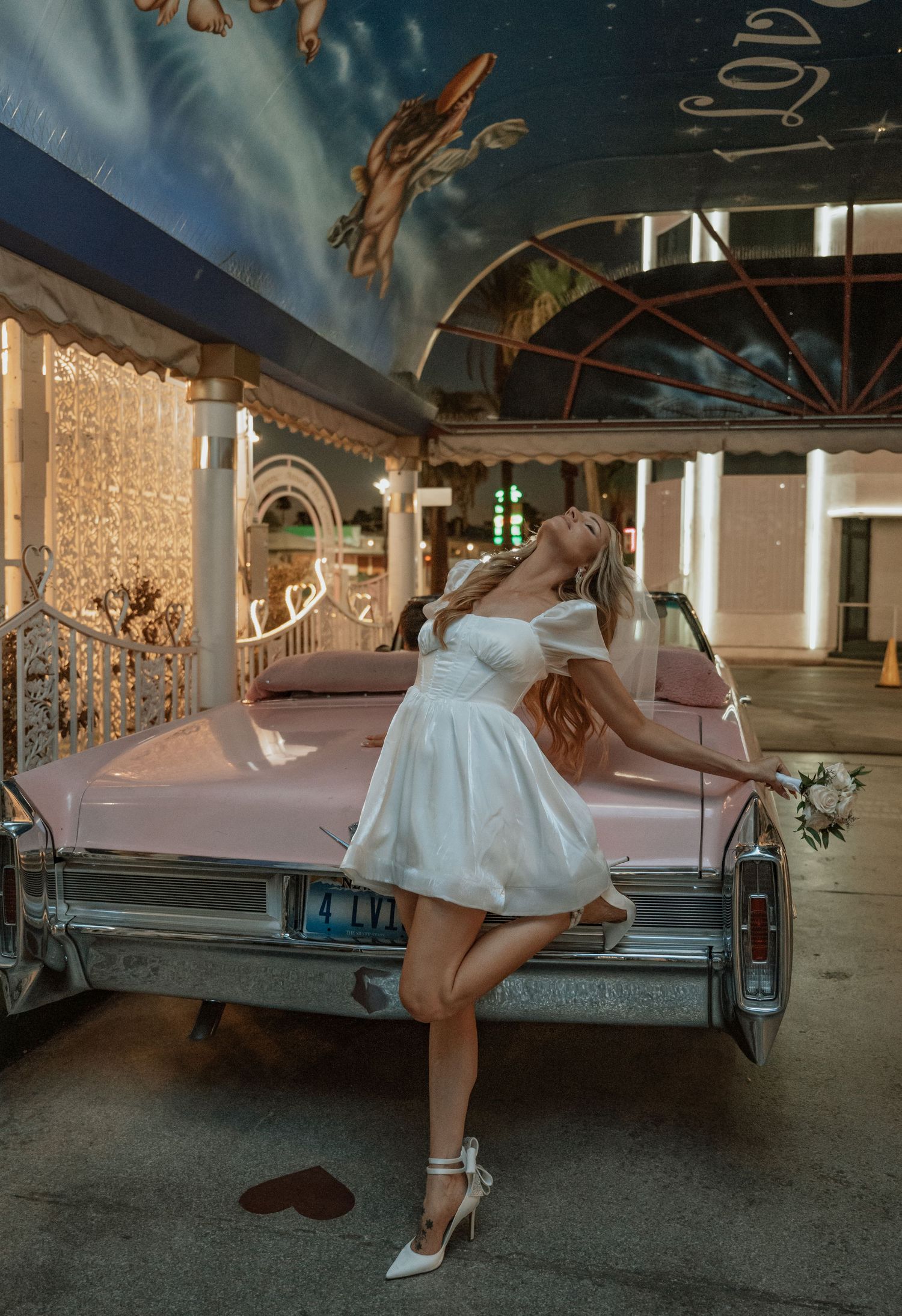 A couple poses with a classic car at night outside a wedding chapel.