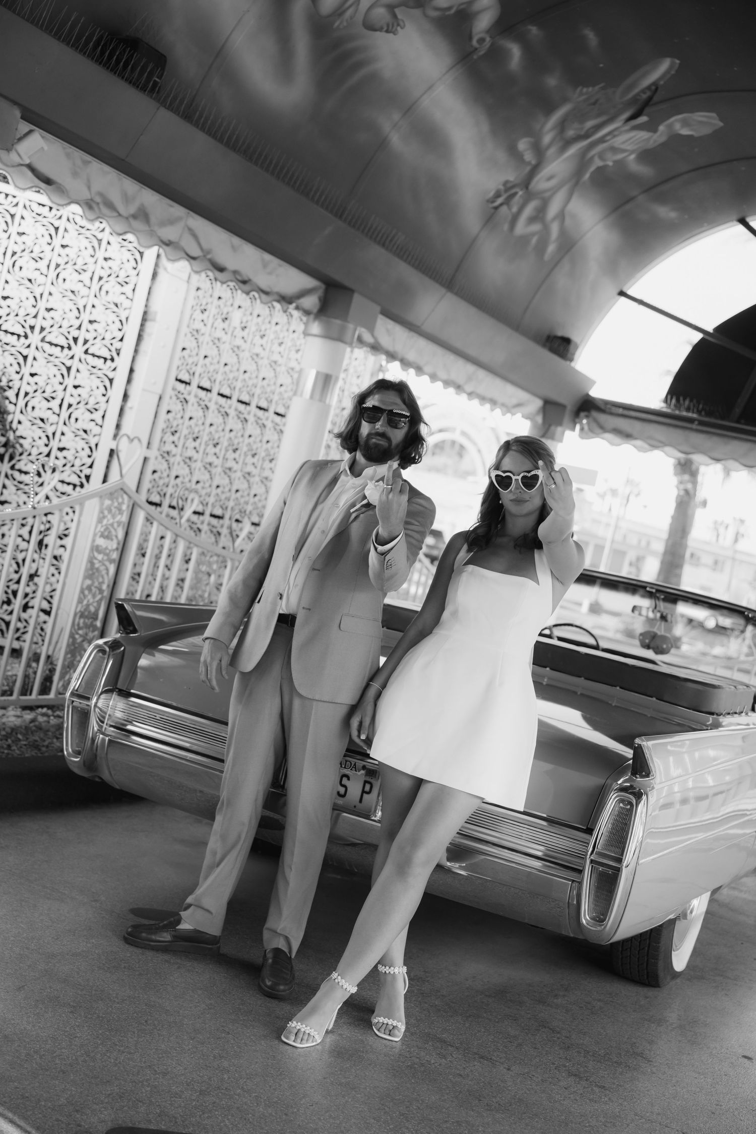 Black and white photo series of a couple sitting beneath a car in casual clothing.
