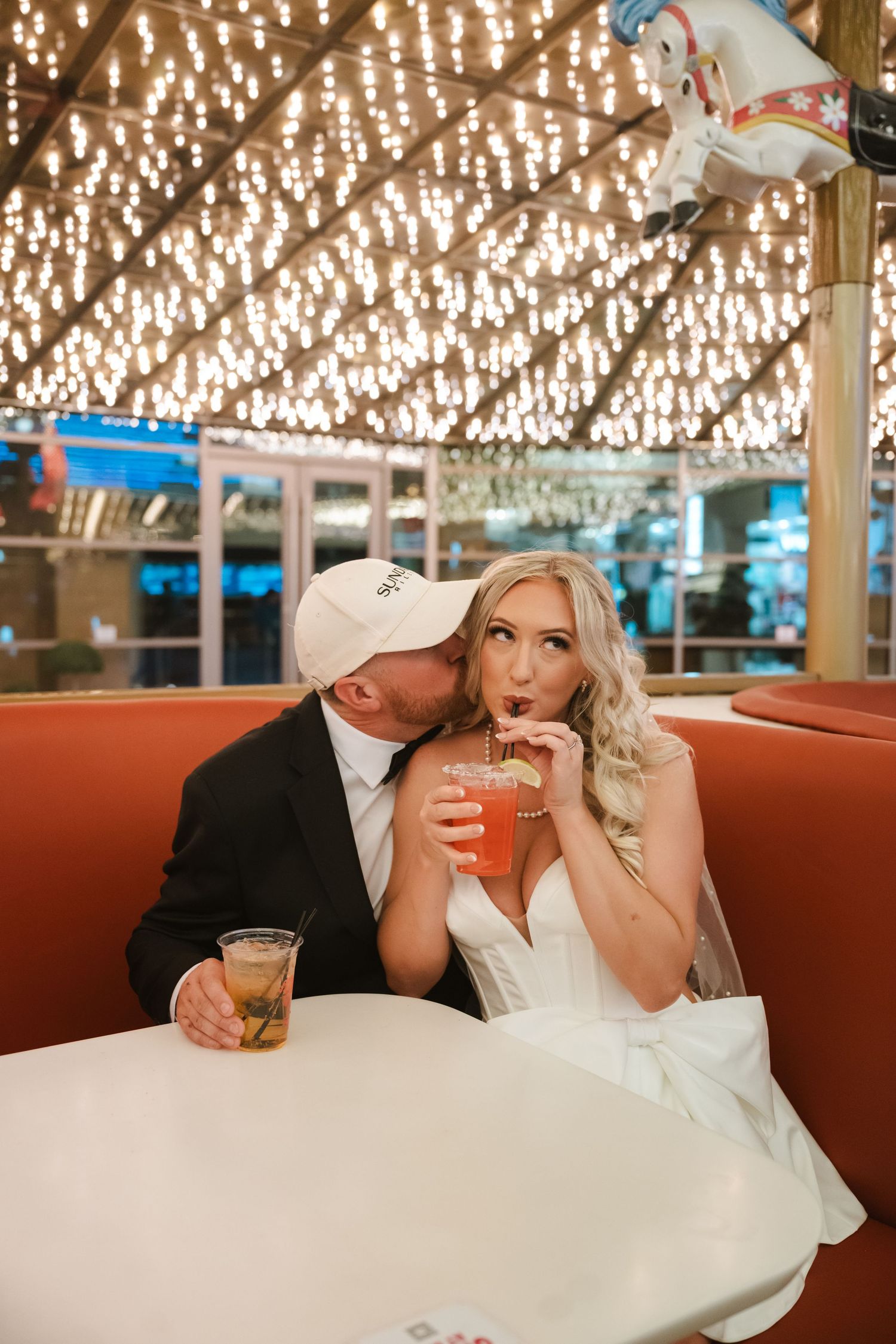 A couple in wedding attire shares intimate moments in a restaurant booth under decorative lighting.