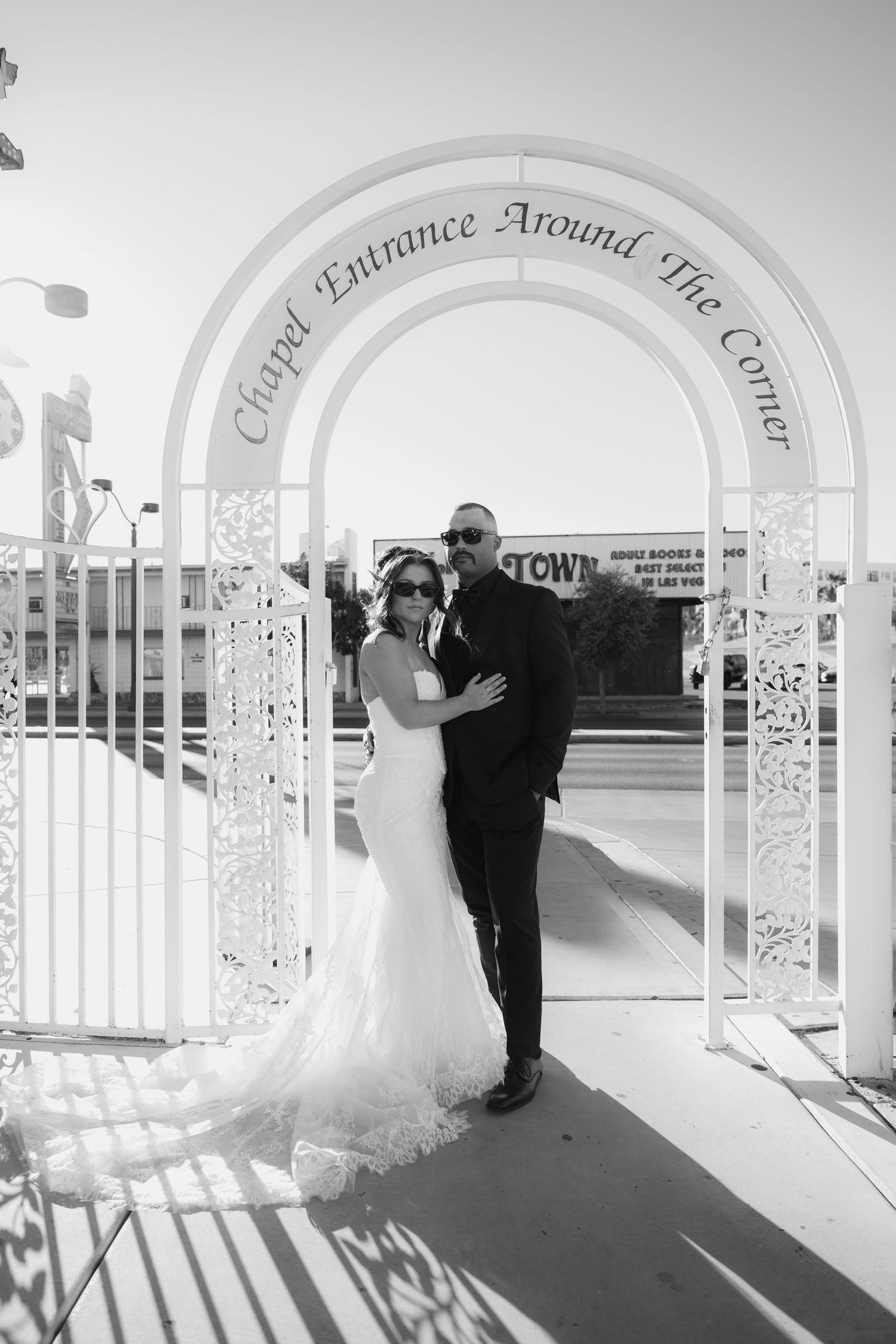 Bride and groom pose under a white chapel arch in Las Vegas, captured in elegant black and white wedding photography.