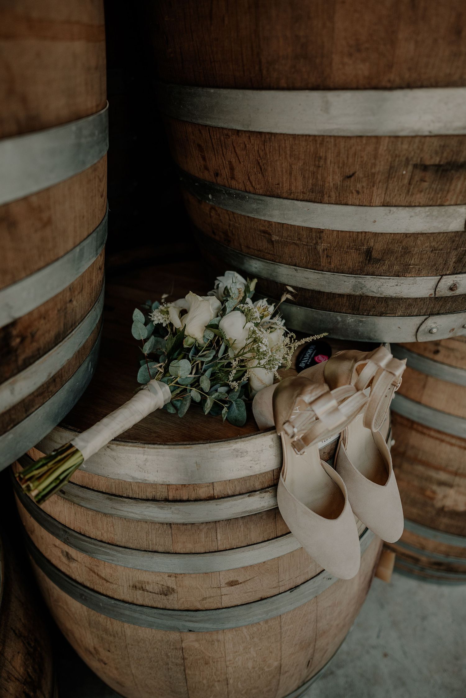 A wedding bouquet and ballet shoes rest on vintage wooden wine barrels.