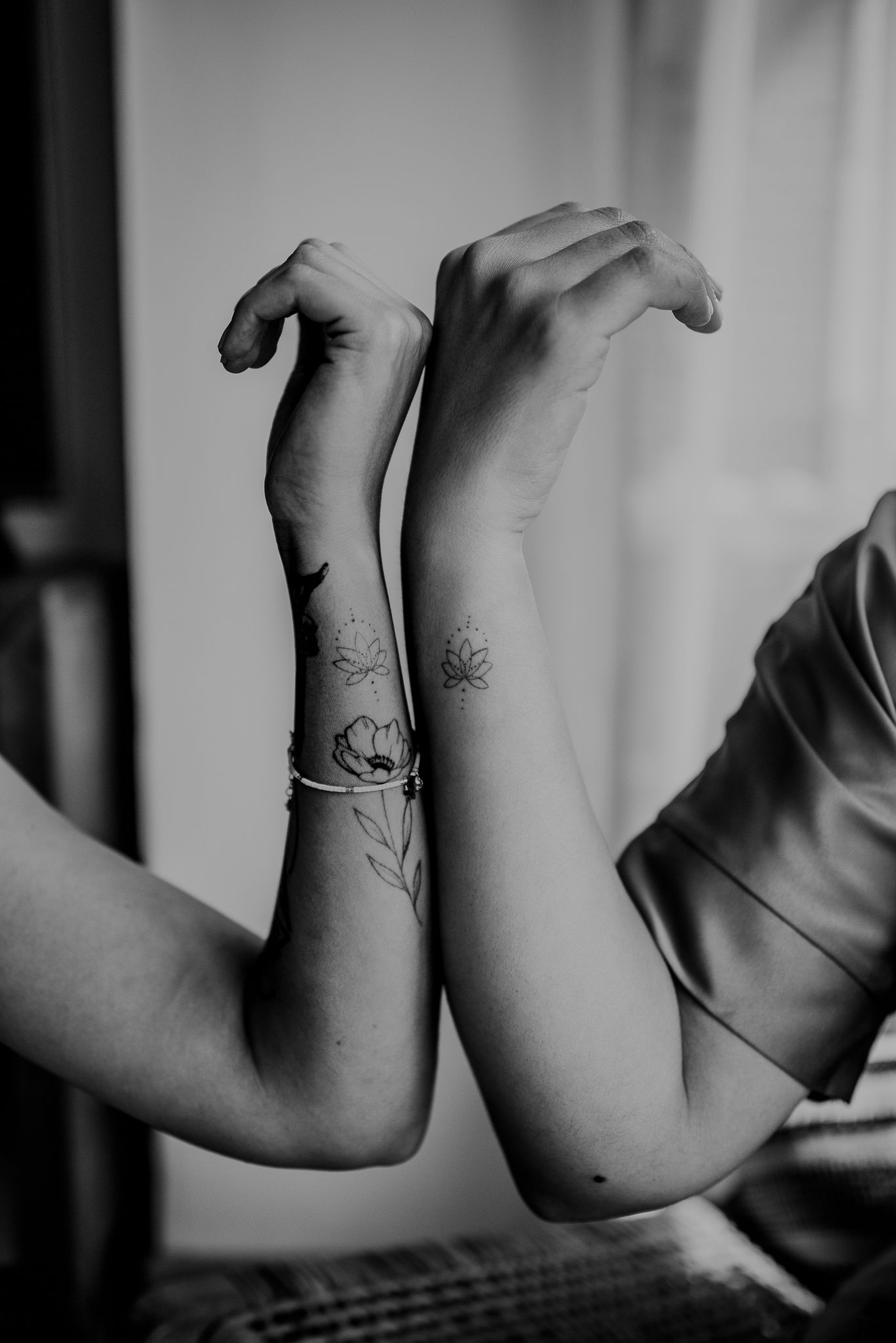 Black and white photo of matching floral tattoos on two arms.