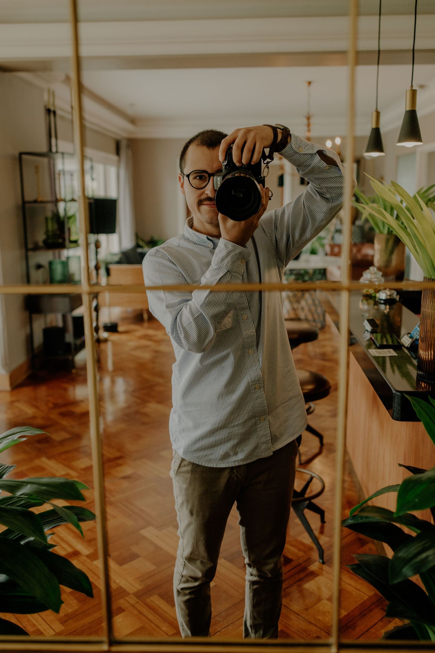 A photographer in a gray sweater demonstrates different camera angles while shooting in a modern interior space.