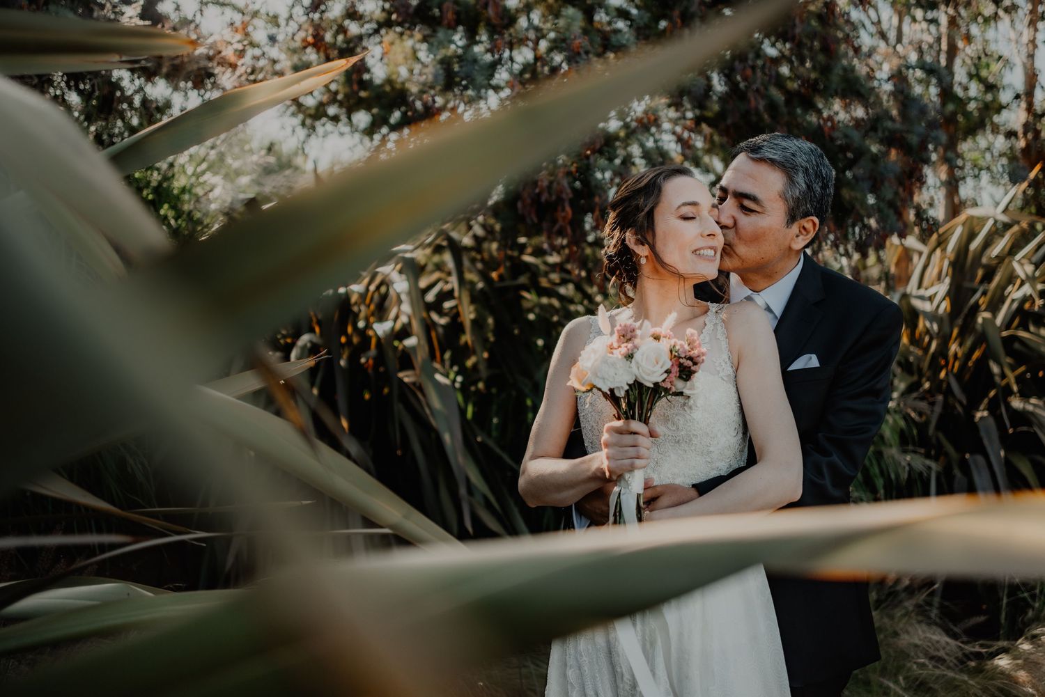 An intimate wedding portrait framed by tropical leaves in natural lighting.