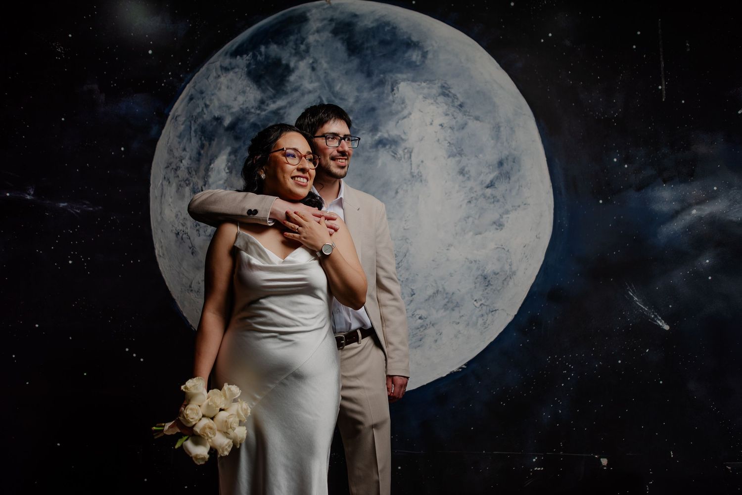 A stylish wedding portrait with a dramatic full moon backdrop and starry sky.