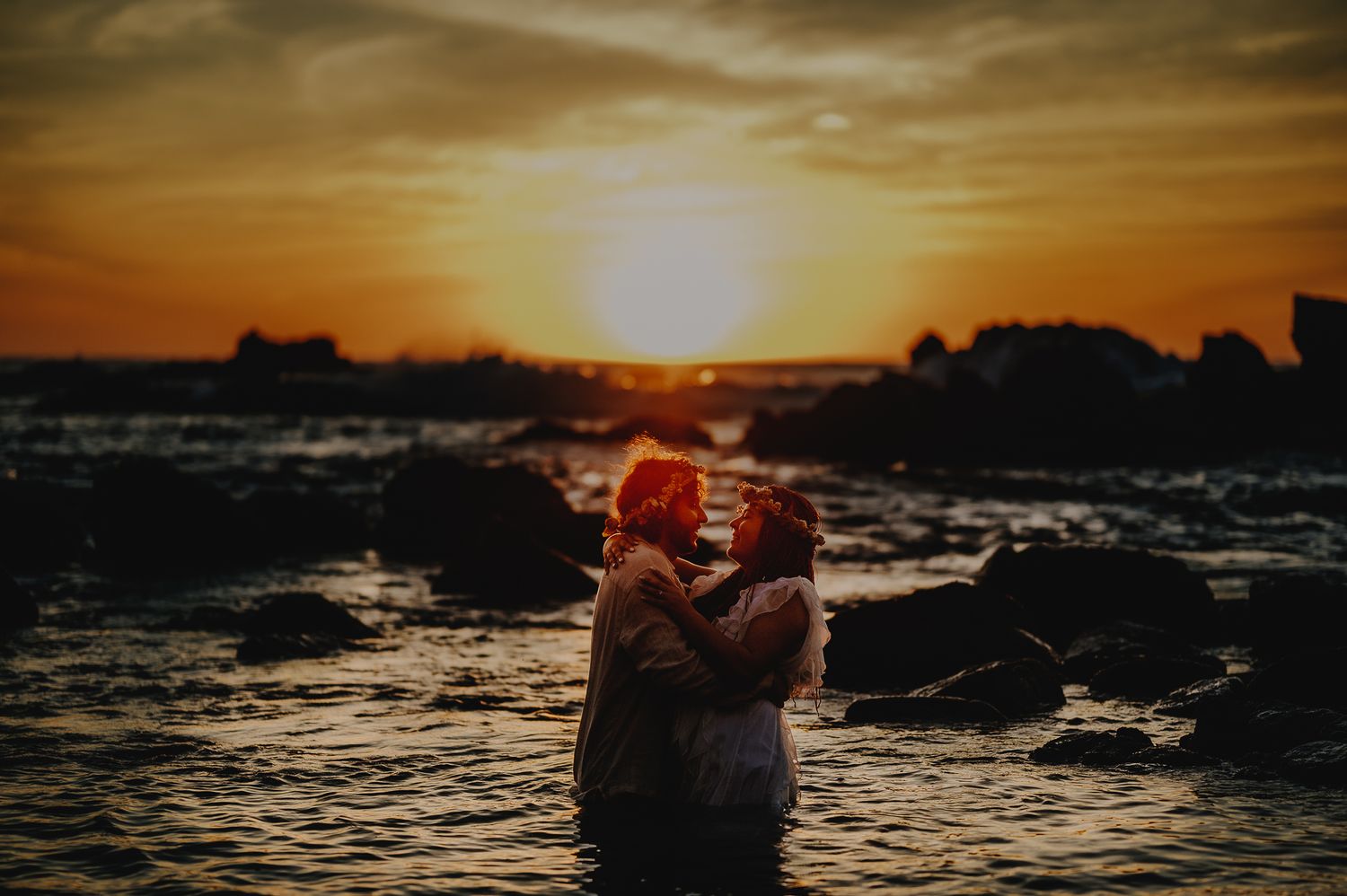 Silhouette of a couple embracing in the ocean during a golden sunset.