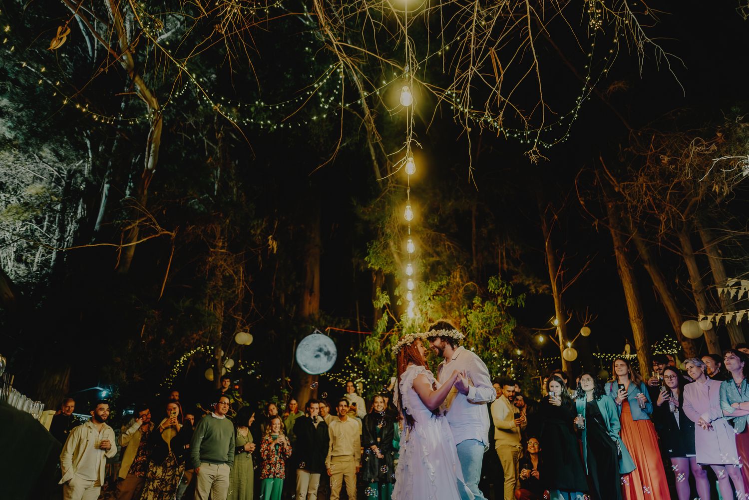 Wedding reception under string lights with guests dancing at an outdoor venue.