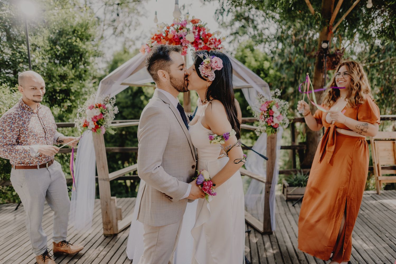 A ceremony moment under a red floral arch with guests in attendance.