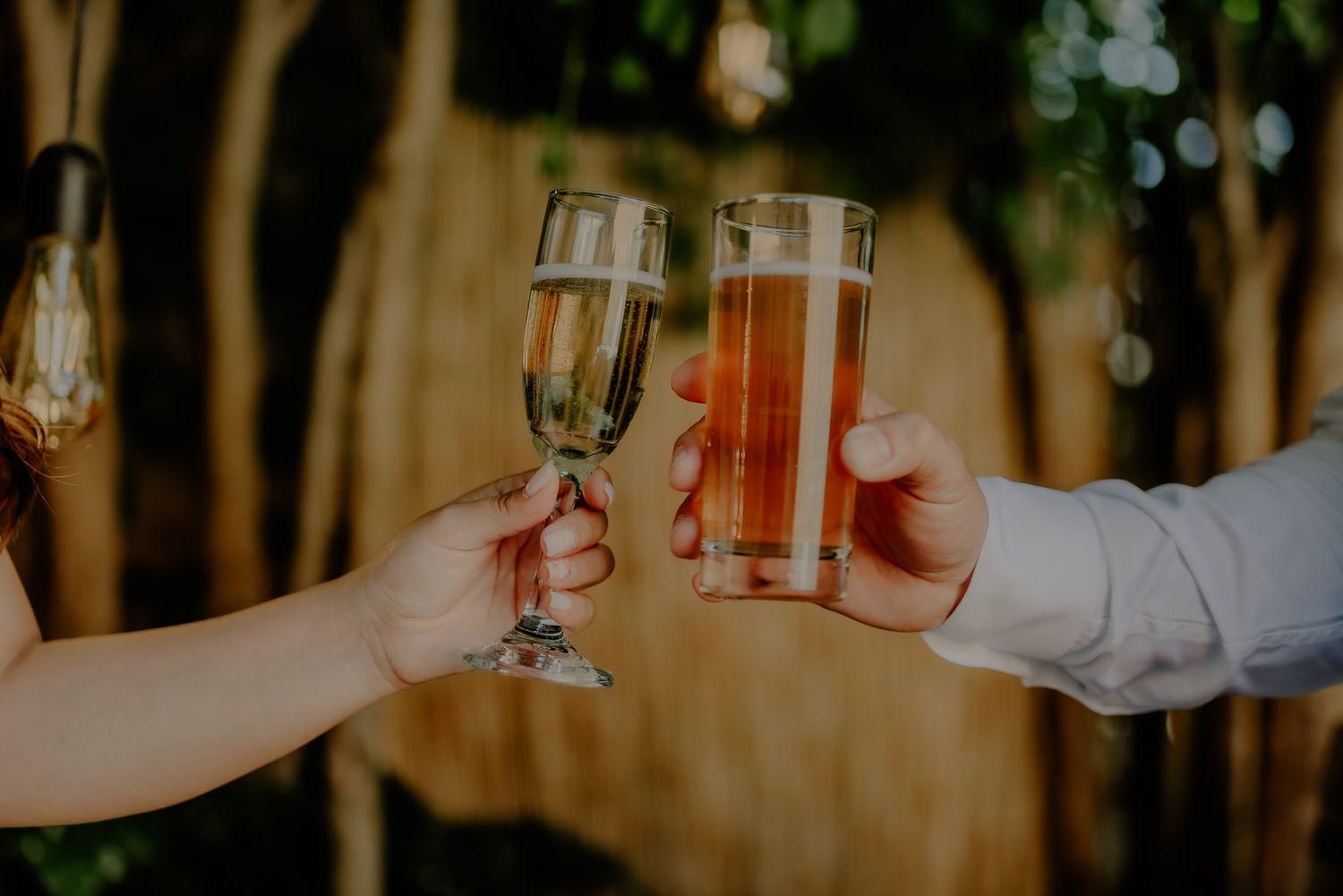 Two hands toasting with champagne and beer glasses at a celebration.