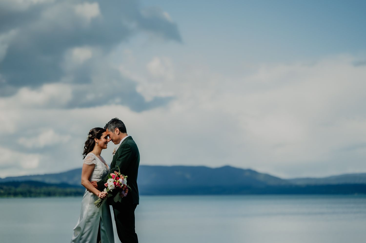 A tender moment between newlyweds against a scenic mountain lake backdrop.