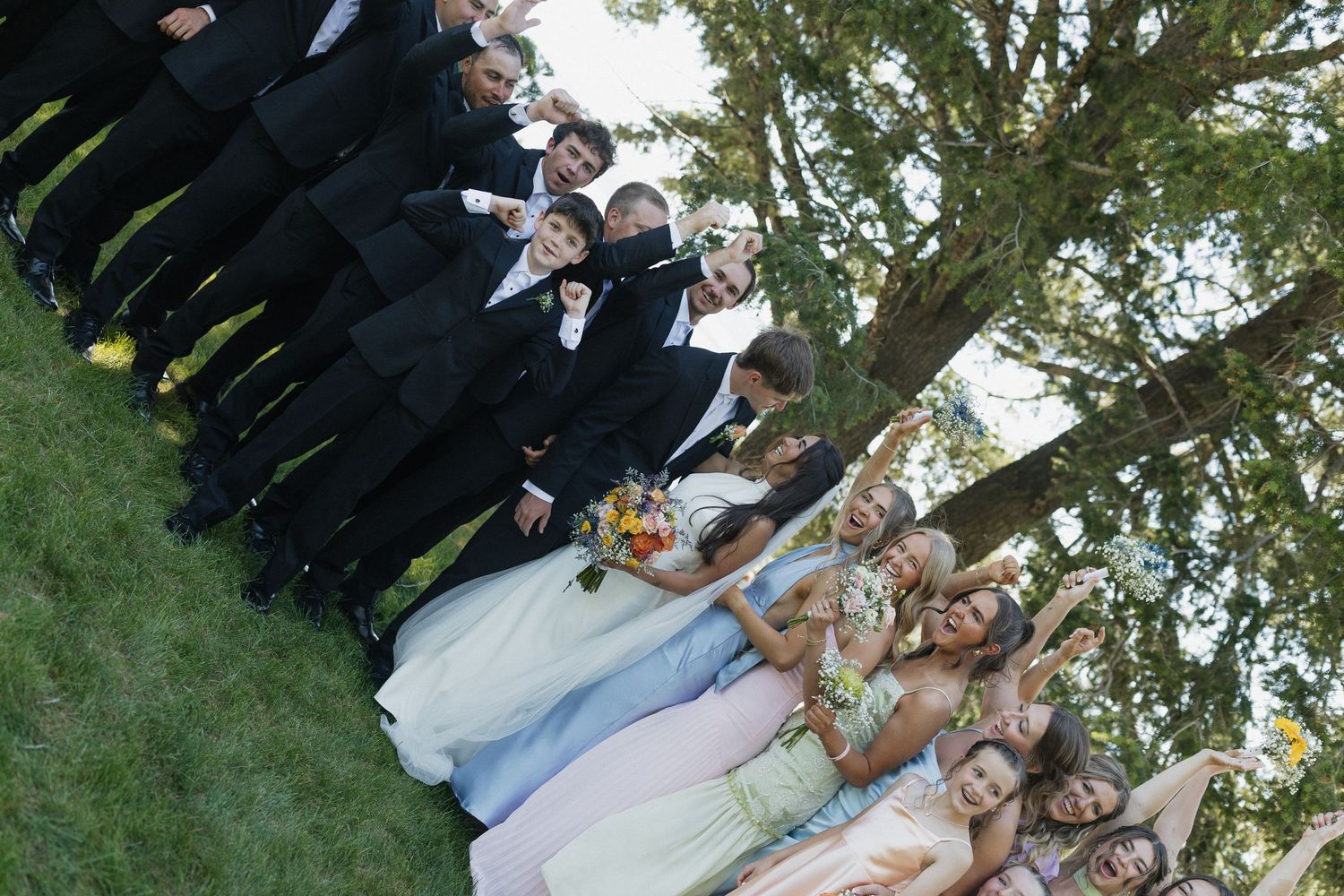 Family and friends gather outdoors in front of trees for group photos at a formal celebration event.