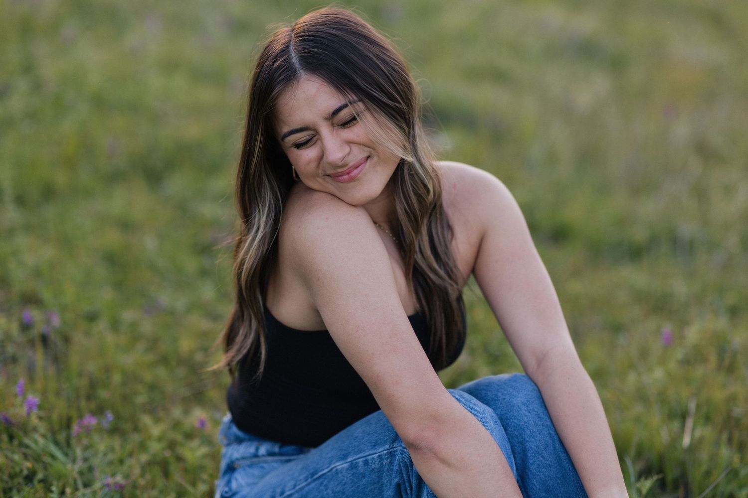 Candid outdoor portrait of someone wearing a black top and jeans while sitting in a grassy field.