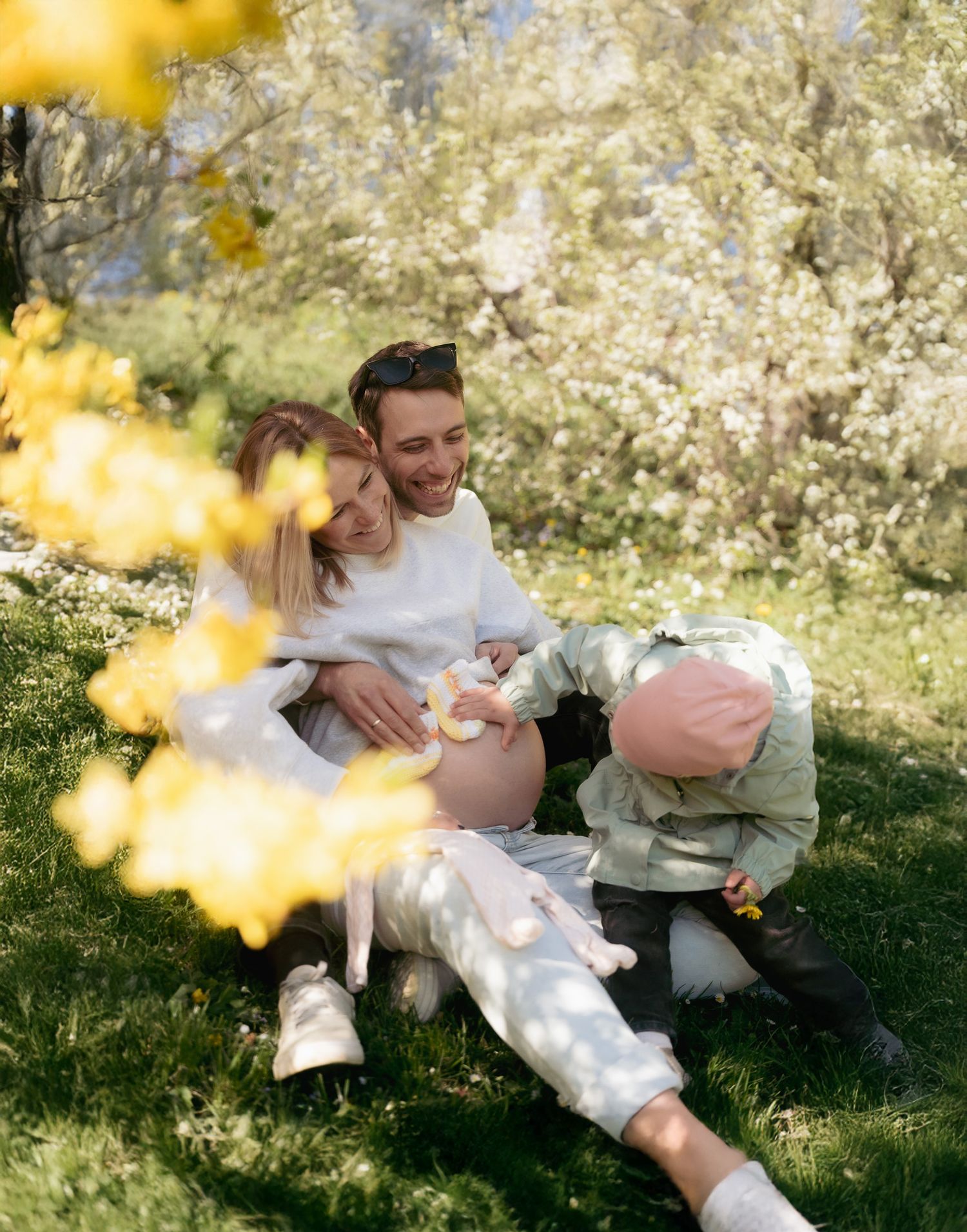 A person relaxes on a grassy hill surrounded by blooming white flowers and dappled sunlight on a spring day.