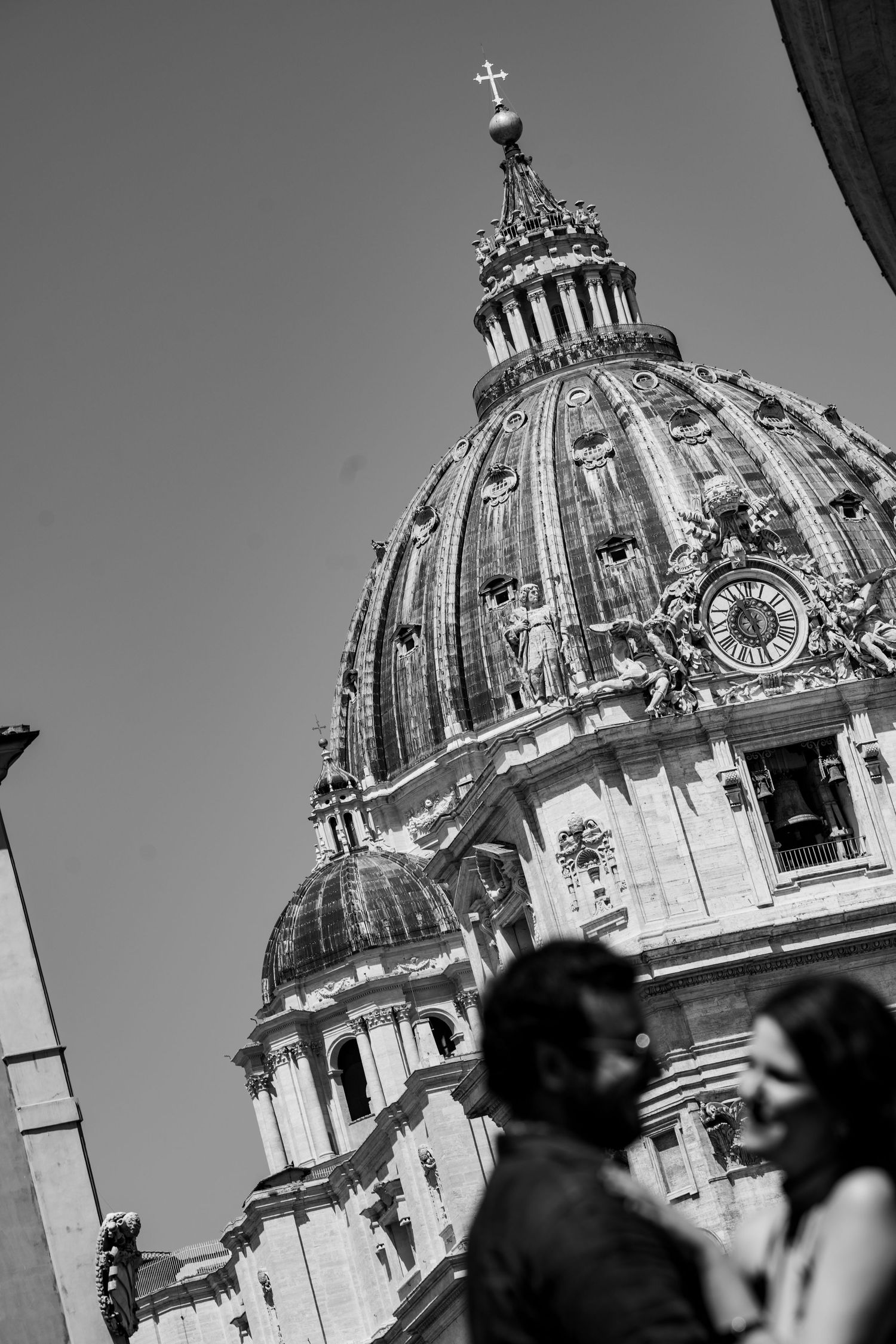 Black and white photo of a couple in front of St. Peter's Basilica dome in Vatican City, Rome.