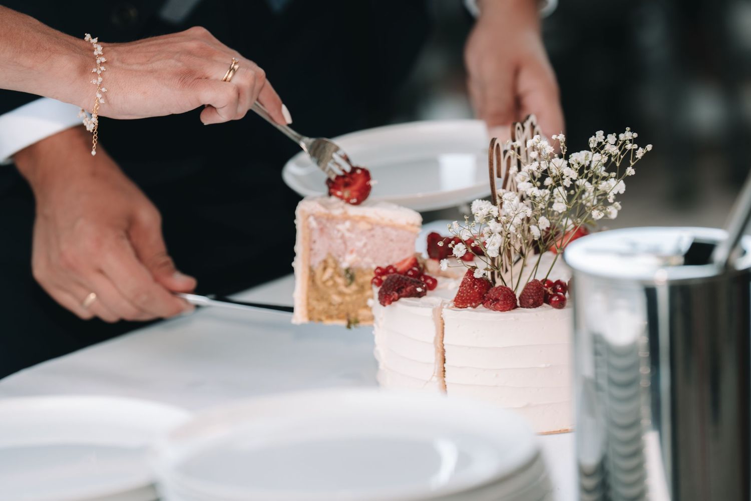 Couple cutting a white wedding cake topped with fresh strawberries and delicate dried flowers at a reception.