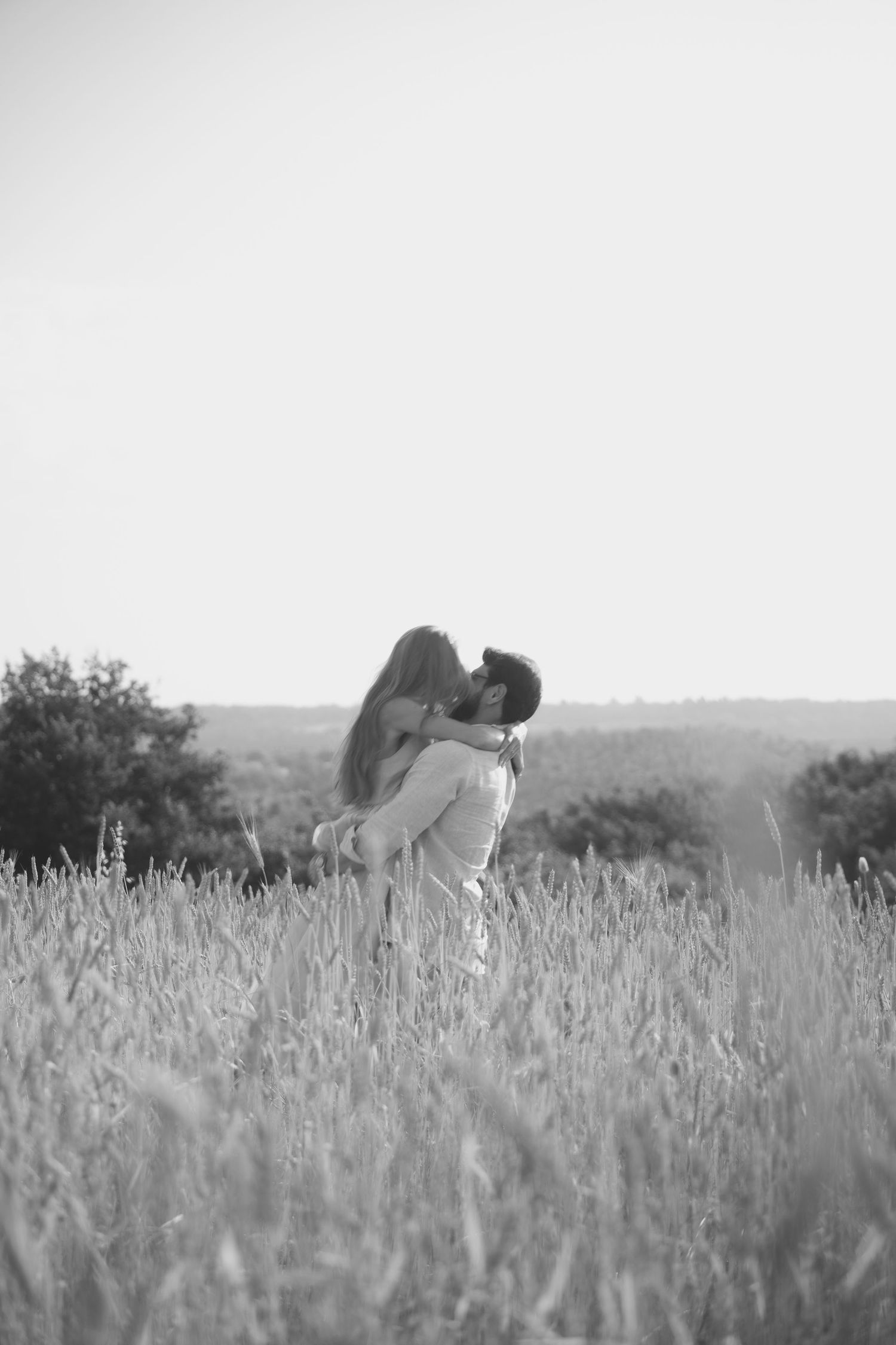 A romantic couple embraces in a sunlit field of tall grass during golden hour, shown in three sequential black and white photos.