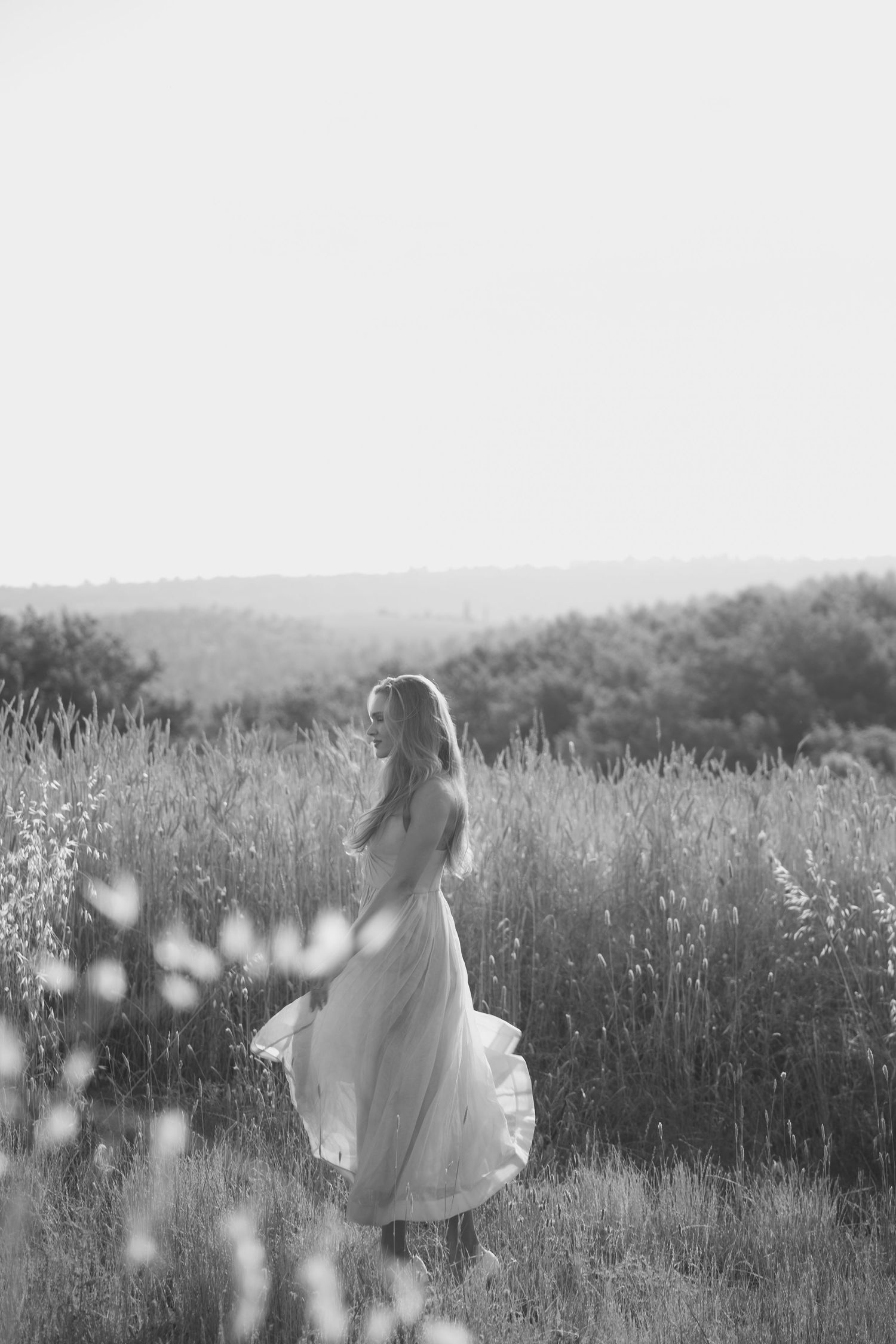 A dreamy black and white photo series shows a person in a white dress twirling through a sunlit meadow of tall grass.