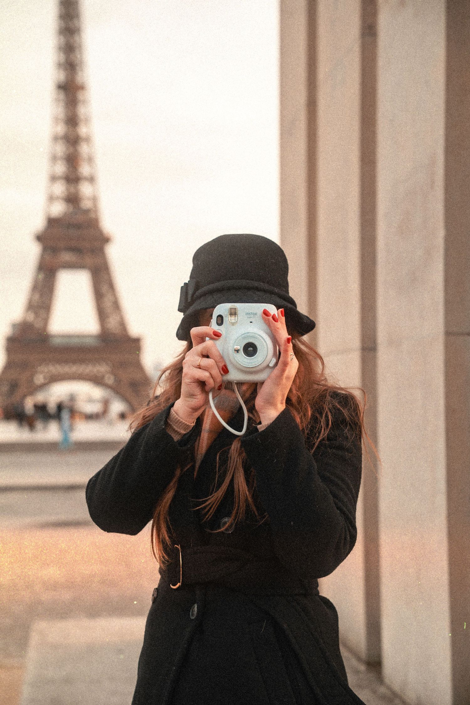 A photographer in black winter attire captures moments near the Eiffel Tower in Paris.