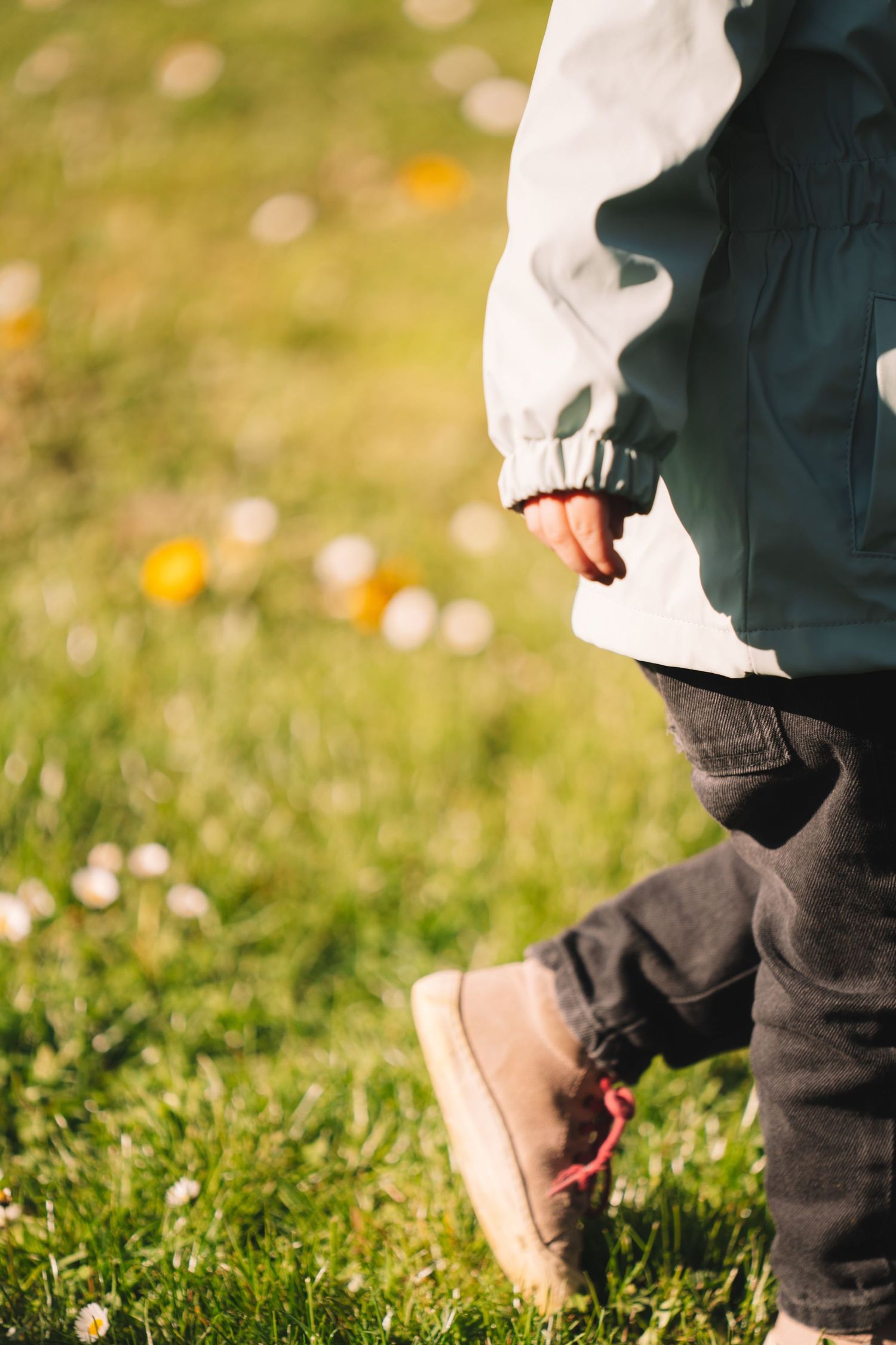 Close-up sequence of feet walking through grass with yellow flowers and sunlit bokeh background.
