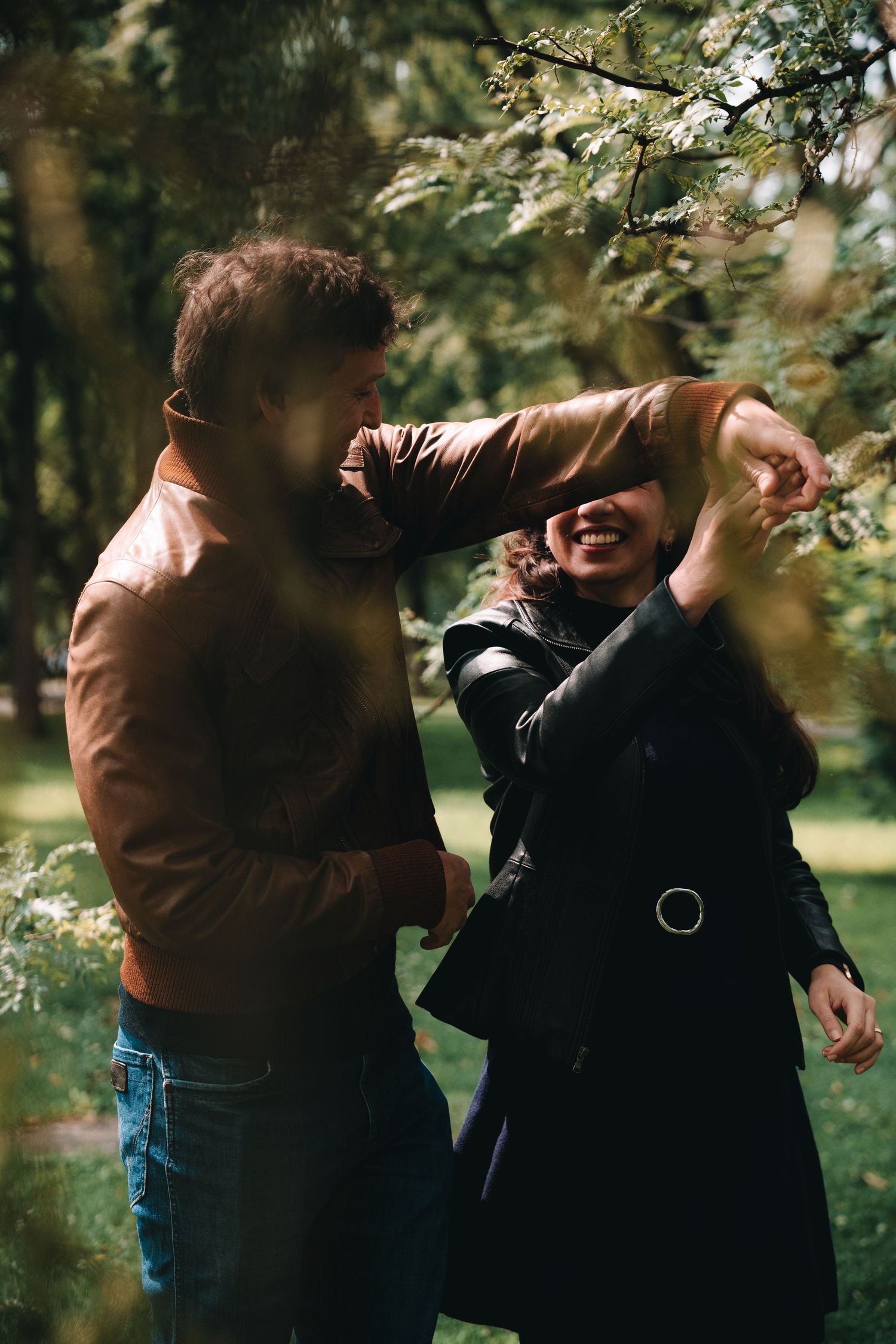 A joyful moment captured between two people in a park with blooming trees and natural lighting.