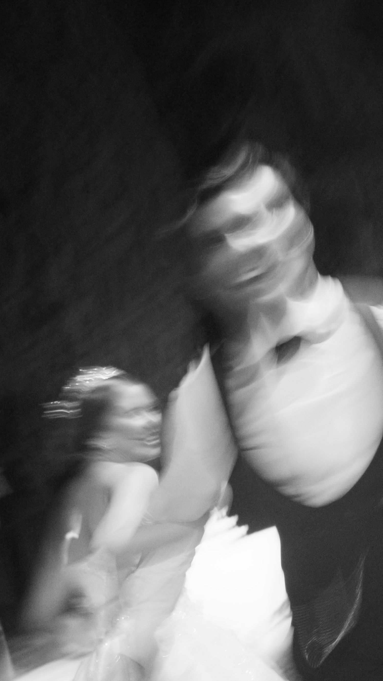Blurry black and white motion blur photo of two people dancing or moving together in low light.