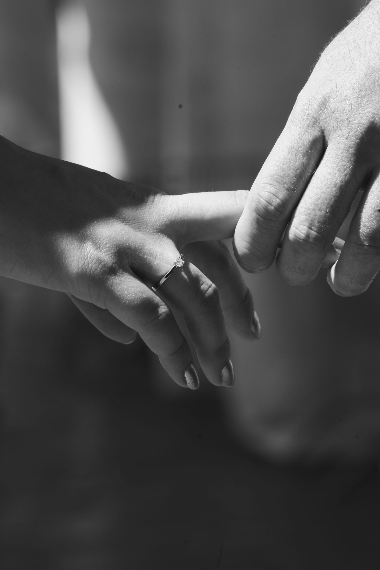 Black and white photo of two hands touching, each wearing a wedding band, symbolizing marriage and unity.