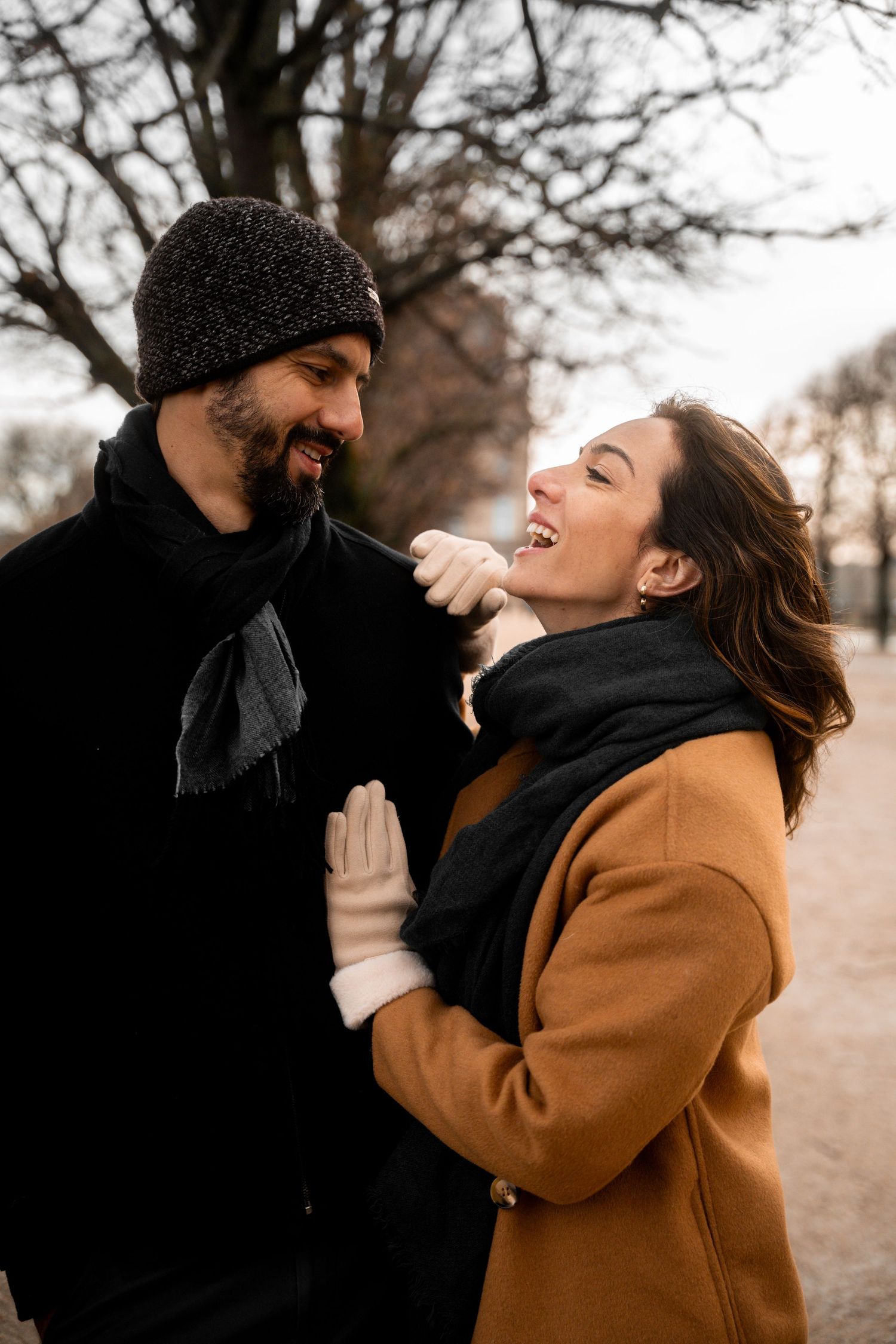 A couple in winter coats share playful laughter and embrace while walking outdoors on a winter day.