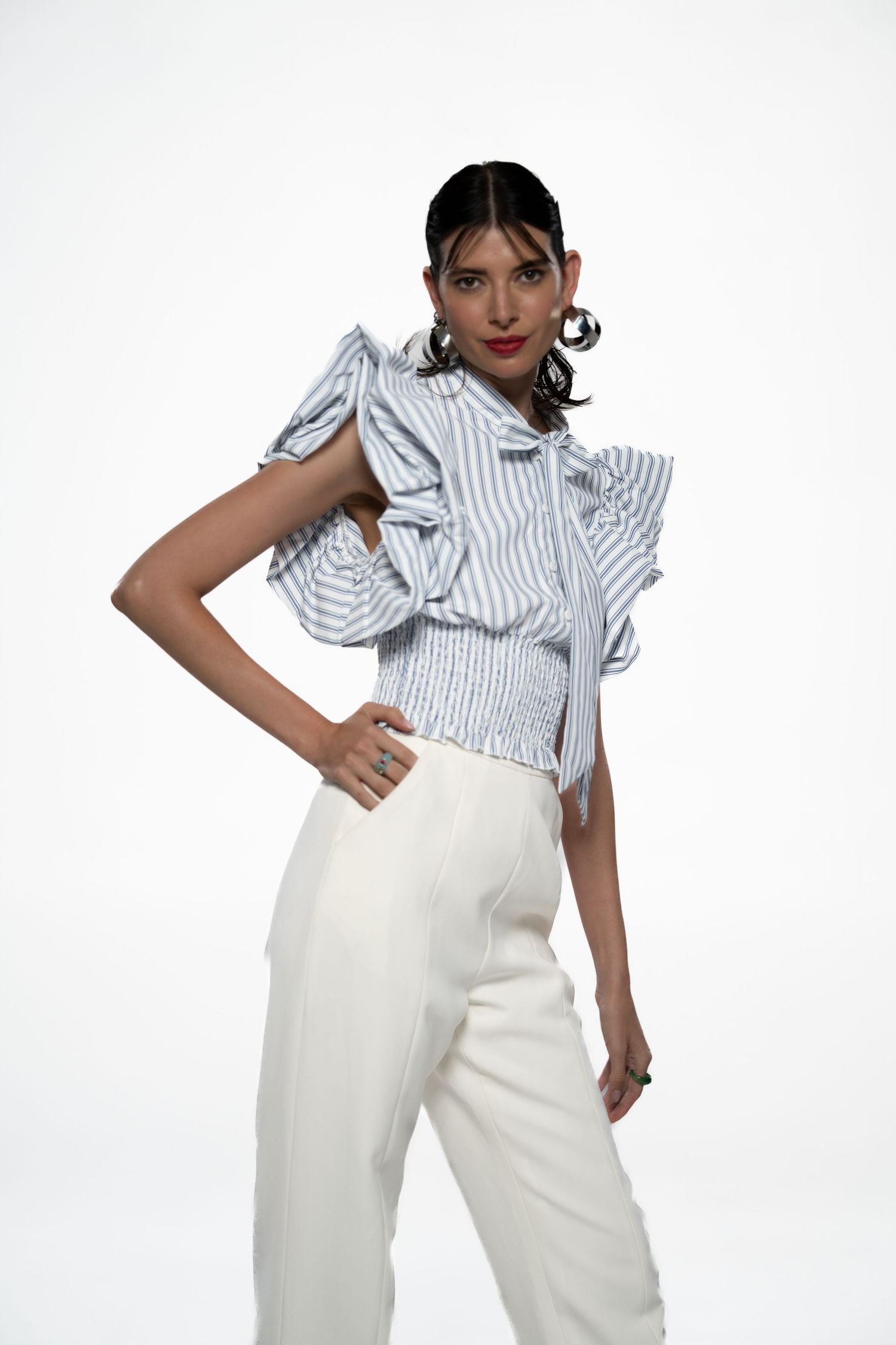 Model poses in ruffled striped blouse and high-waisted white trousers.