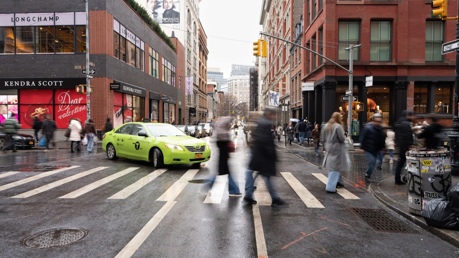 Busy New York City intersection with pedestrians crossing and a bright yellow taxi cab in motion.