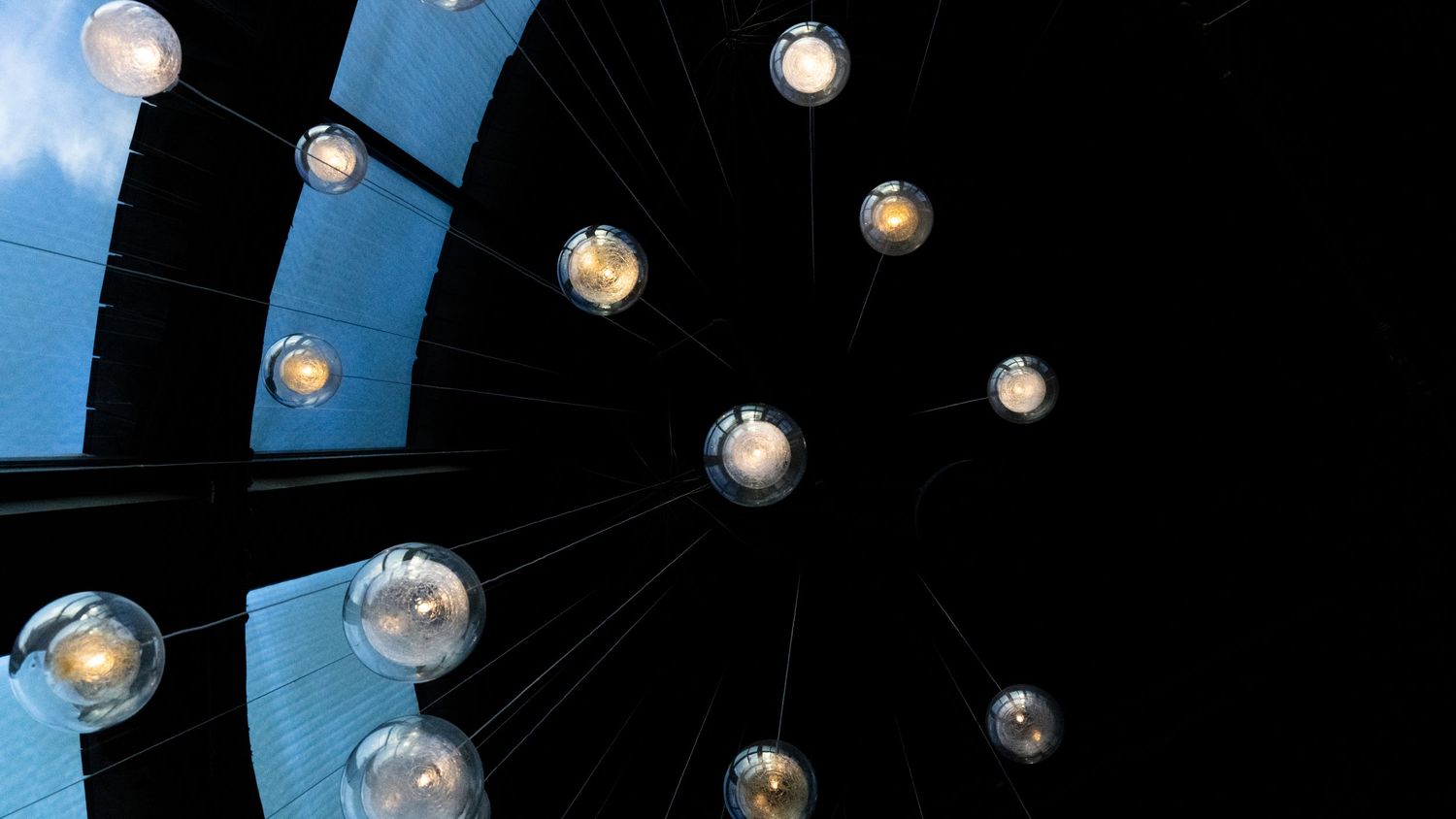 String of illuminated round bulb lights glowing against a dark blue sky.