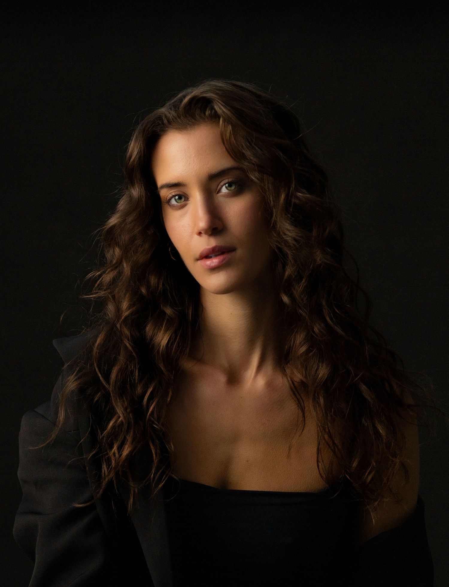 Dramatic portrait against black background with soft lighting and flowing hair.