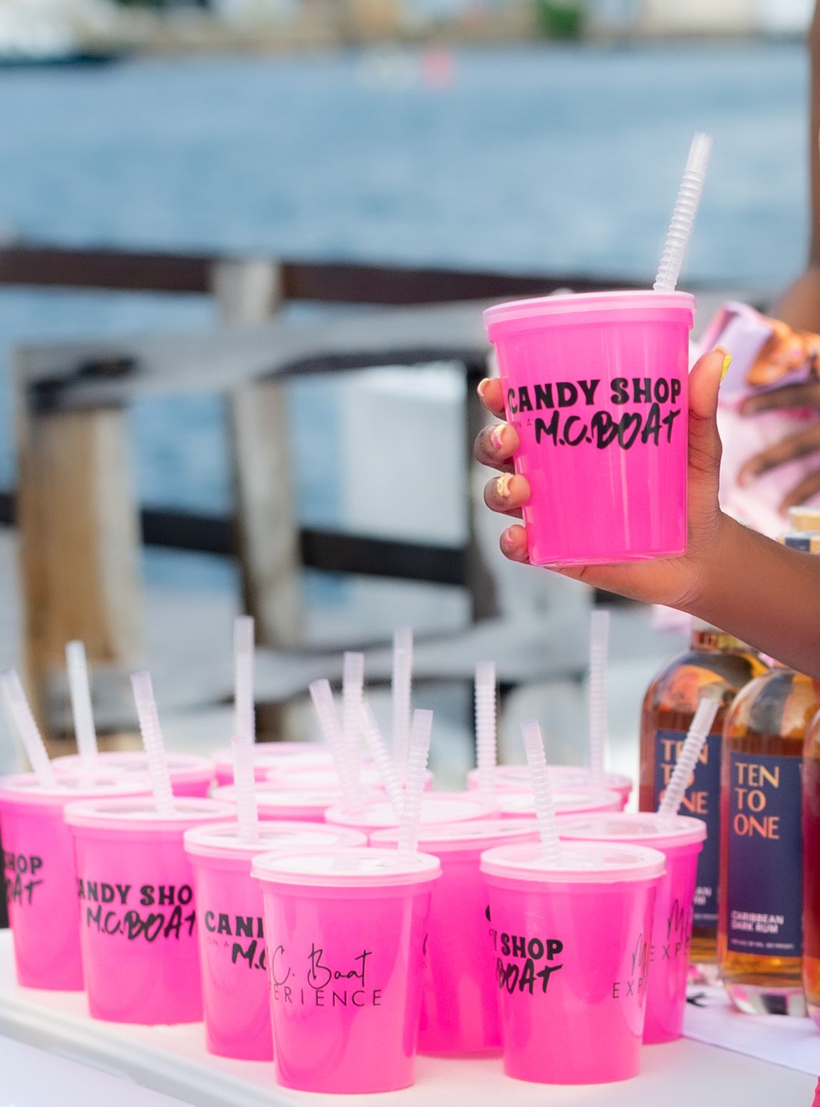 Pink branded party cups with straws arranged on a table with alcohol bottles.