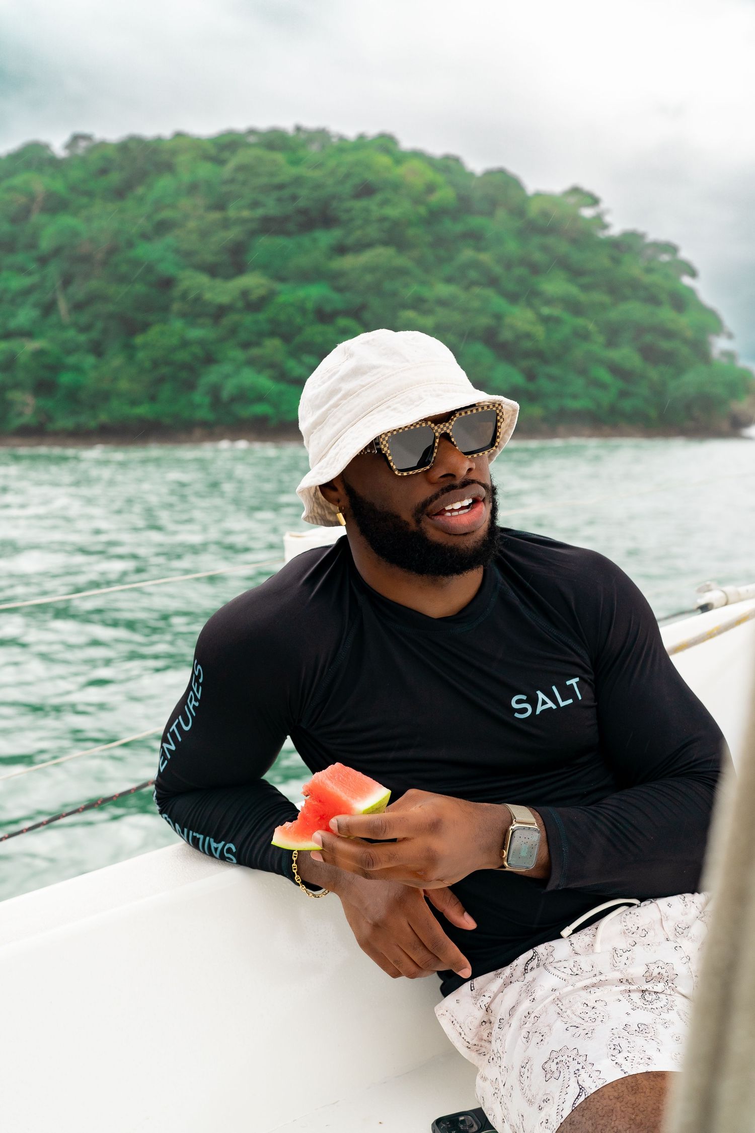 Person in black shirt and white hat enjoying boat ride near tropical island.