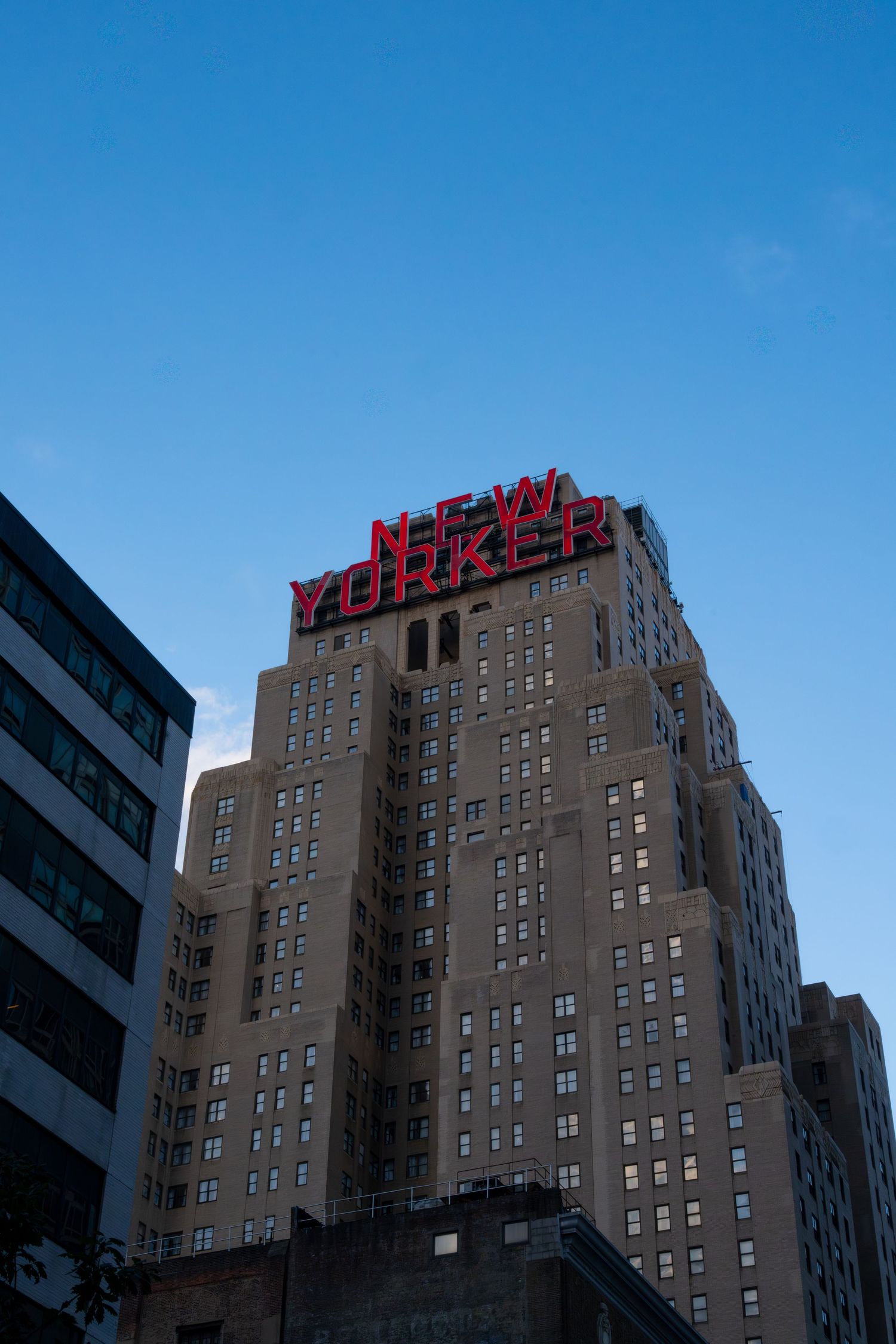 Art deco apartment building with New Yorker sign on top against blue sky.