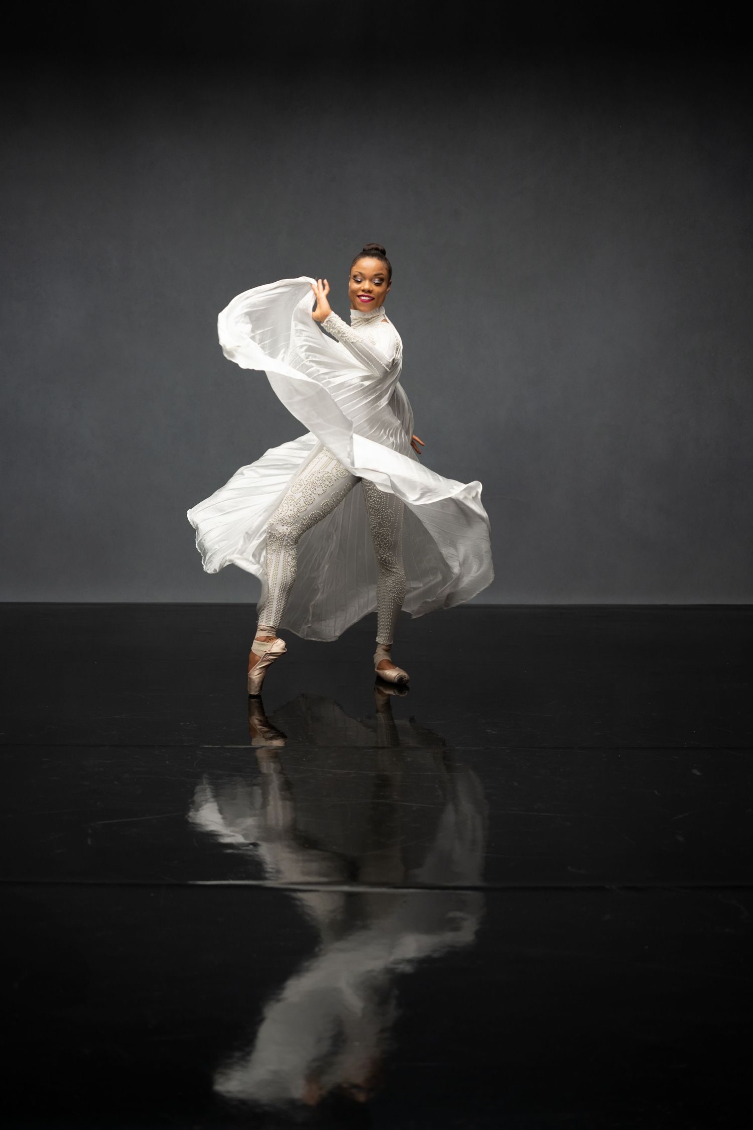 Contemporary dancer in white dress creates dynamic movement on reflective stage surface.