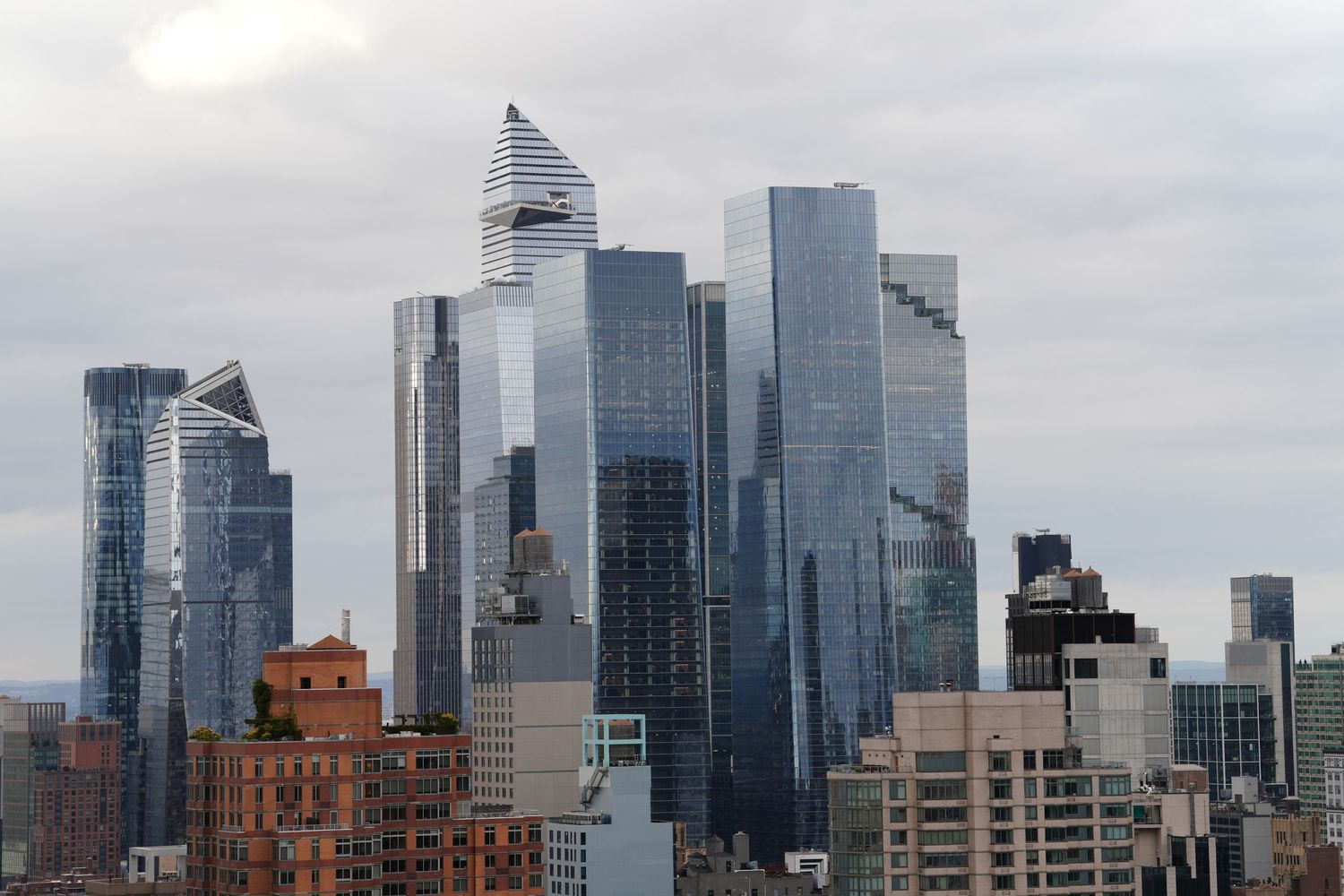 Modern glass skyscrapers and office buildings creating dramatic city skyline against cloudy sky.