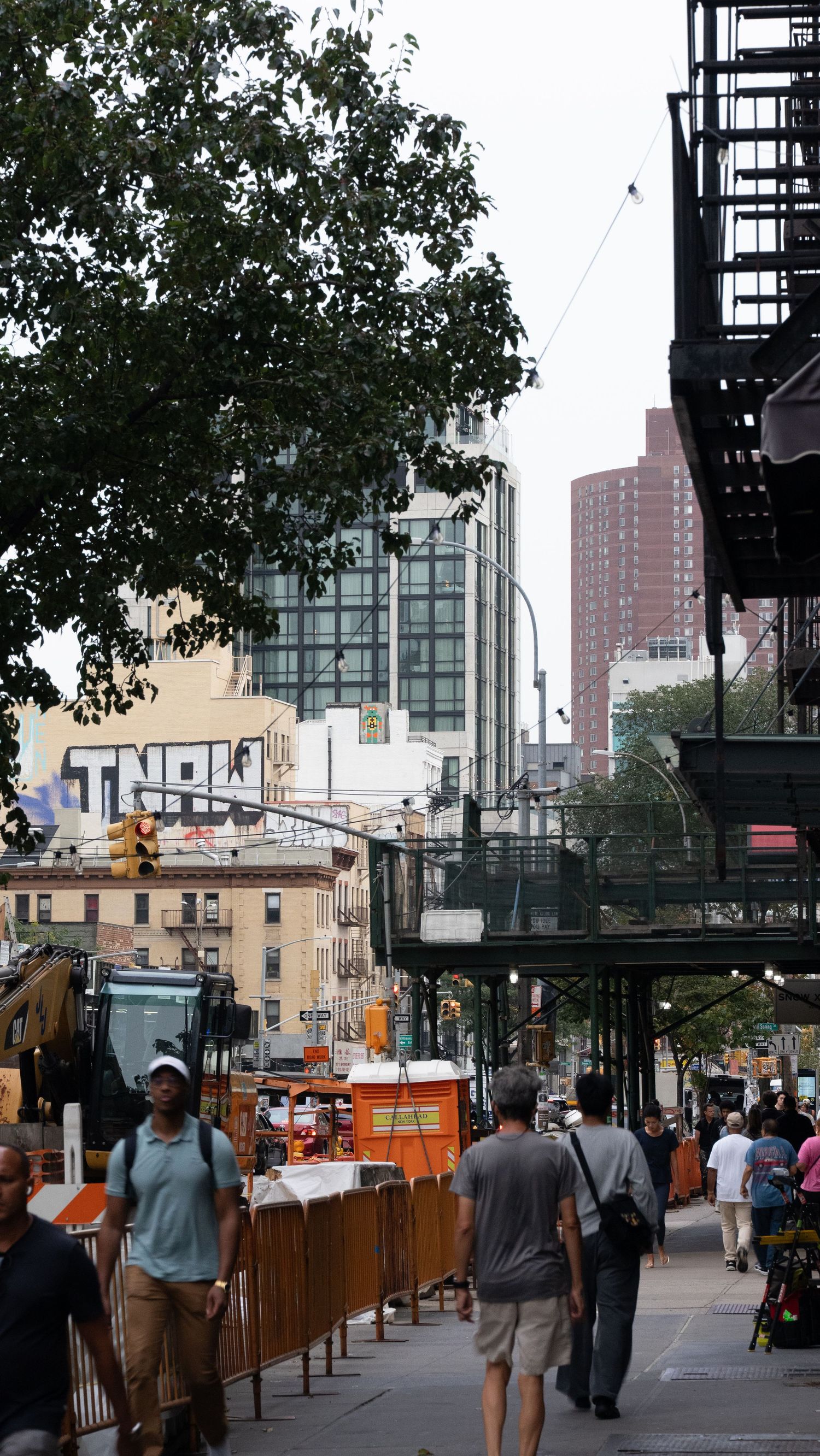 City street with vendors, trees, and tall buildings visible under cloudy skies.