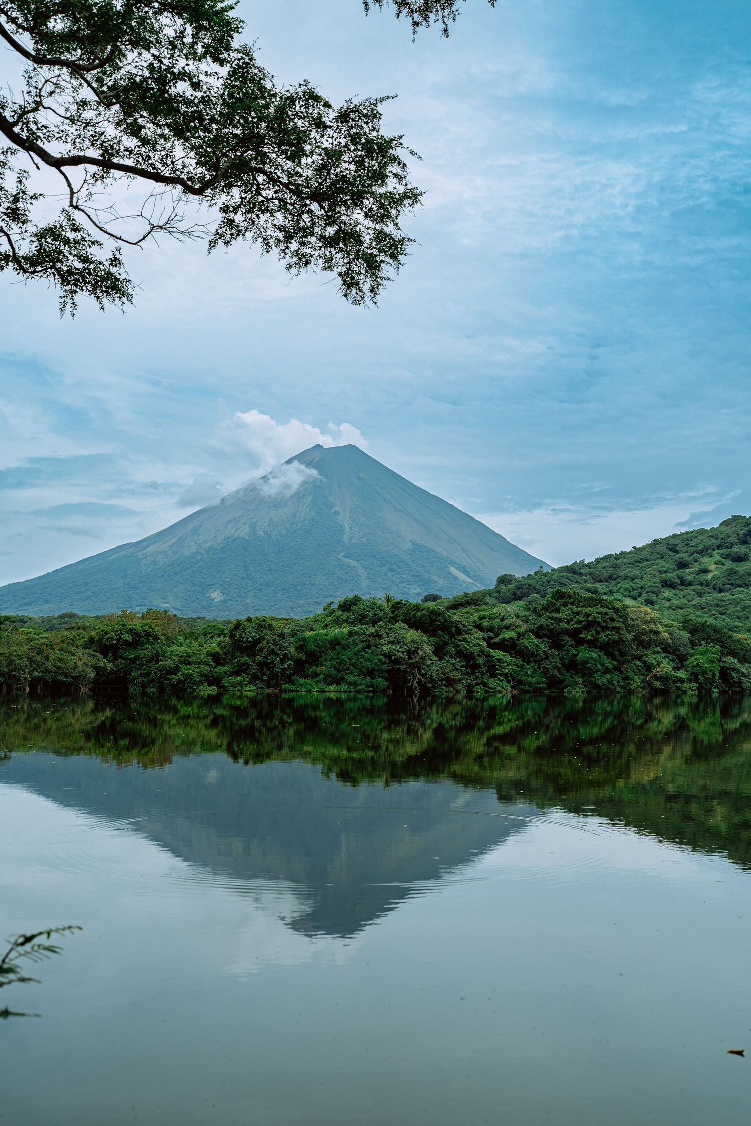 Scenic panoramic view of Ometepe Island's twin volcanoes reflecting in calm lake waters under blue sky in Nicaragua.